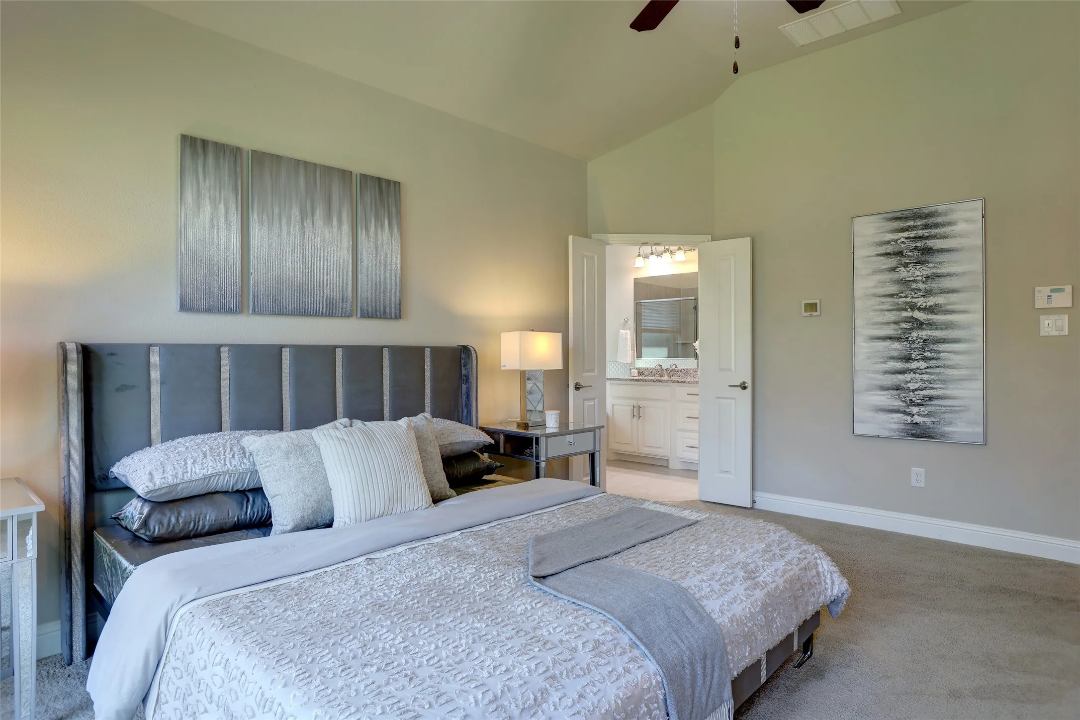 Spacious bedroom featuring vaulted ceilings, plush carpeting, and direct access to a full bathroom