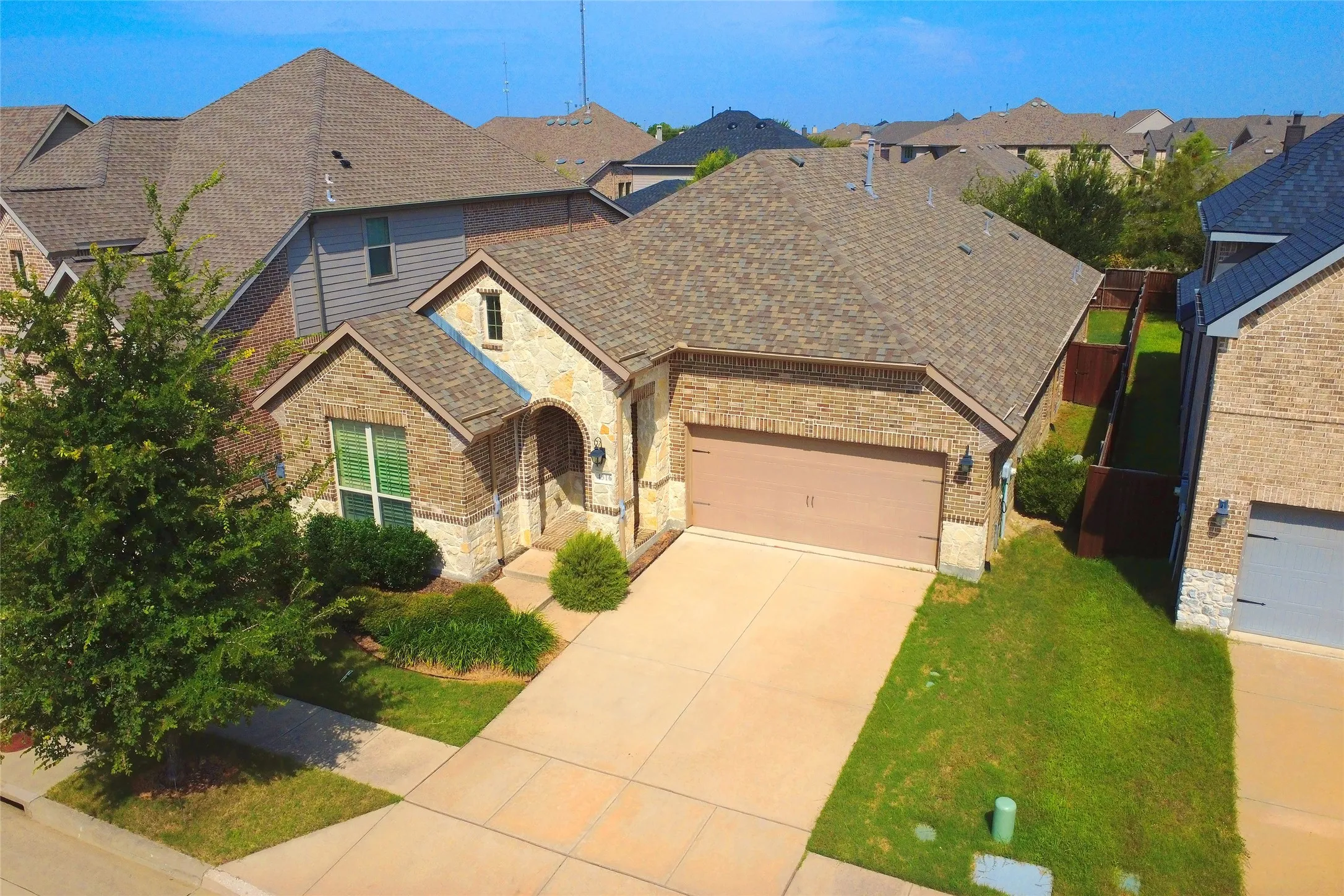 Brick and stone facade residence featuring an arched entryway, attached two-car garage, established front yard landscaping, and a concrete driveway