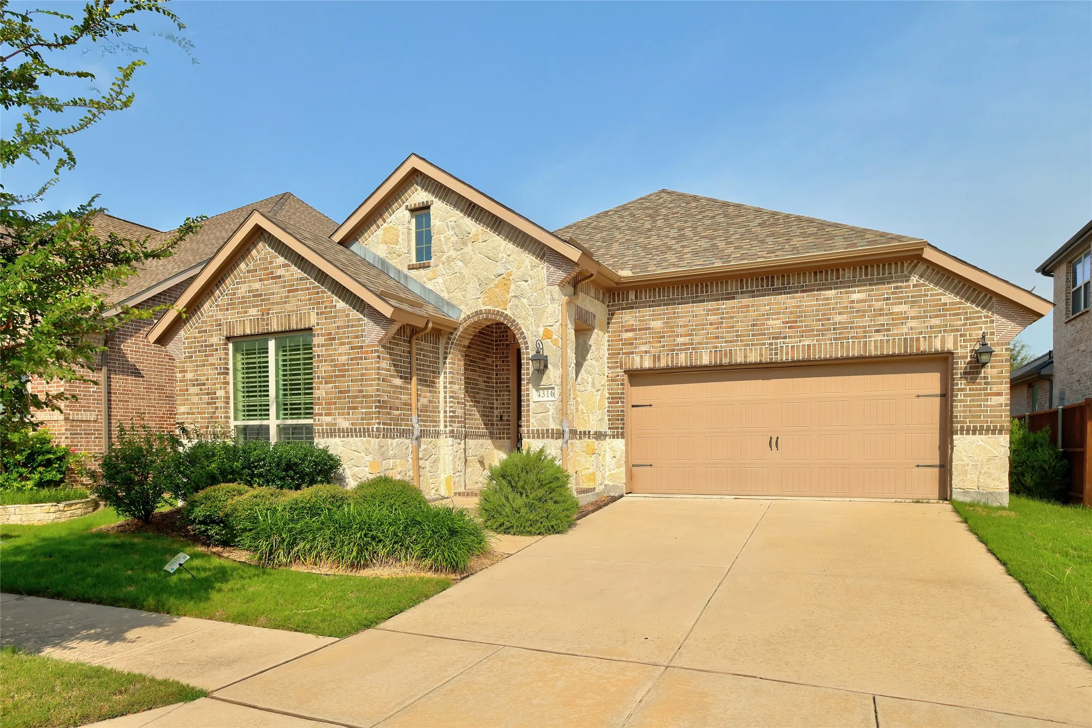 Brick and stone-veneer exterior featuring a gabled roofline, an arched entryway, and a two-car garage with a concrete driveway