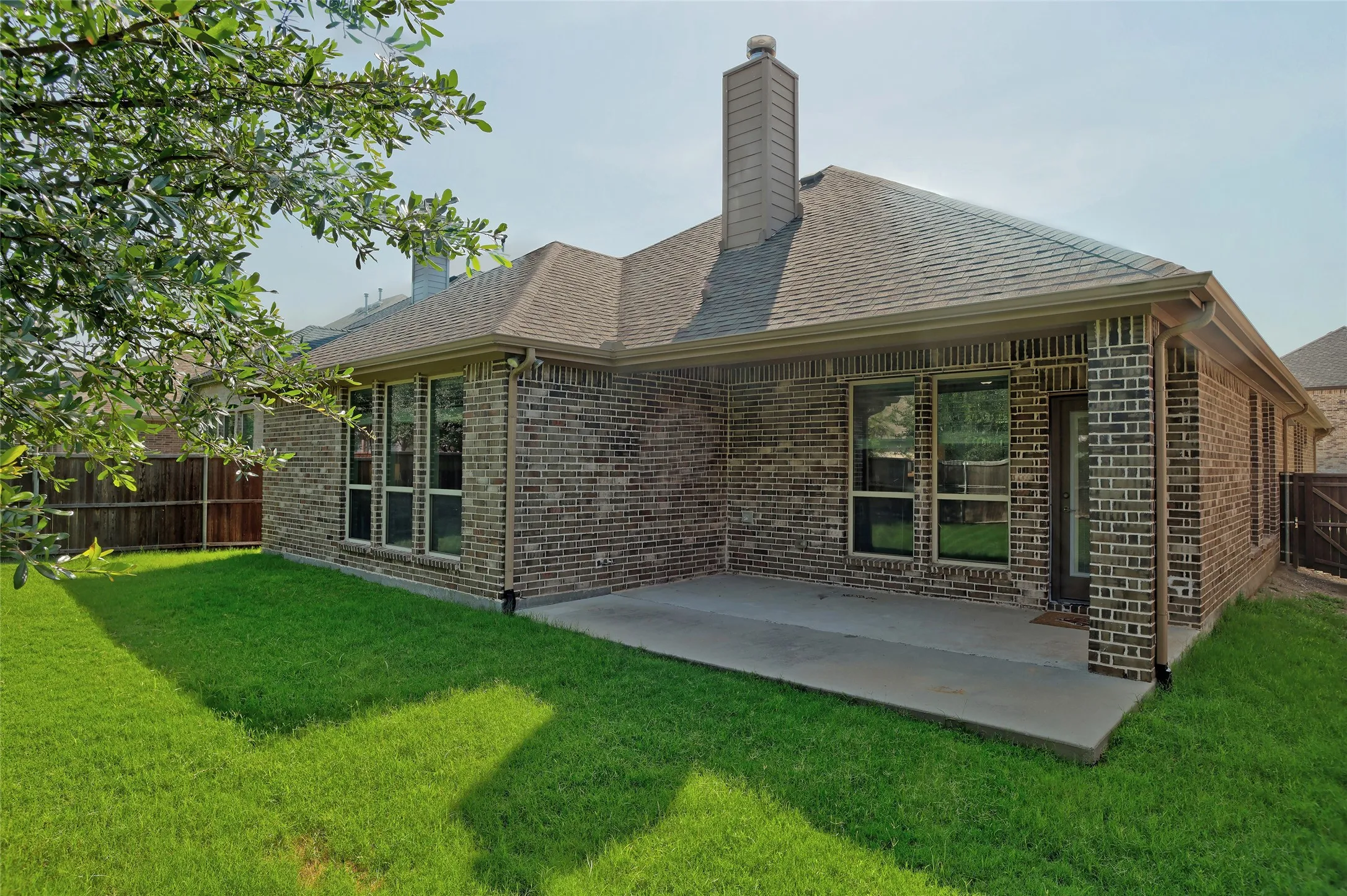 Rear exterior featuring brick facade, covered patio, multiple windows, and a wood privacy fence