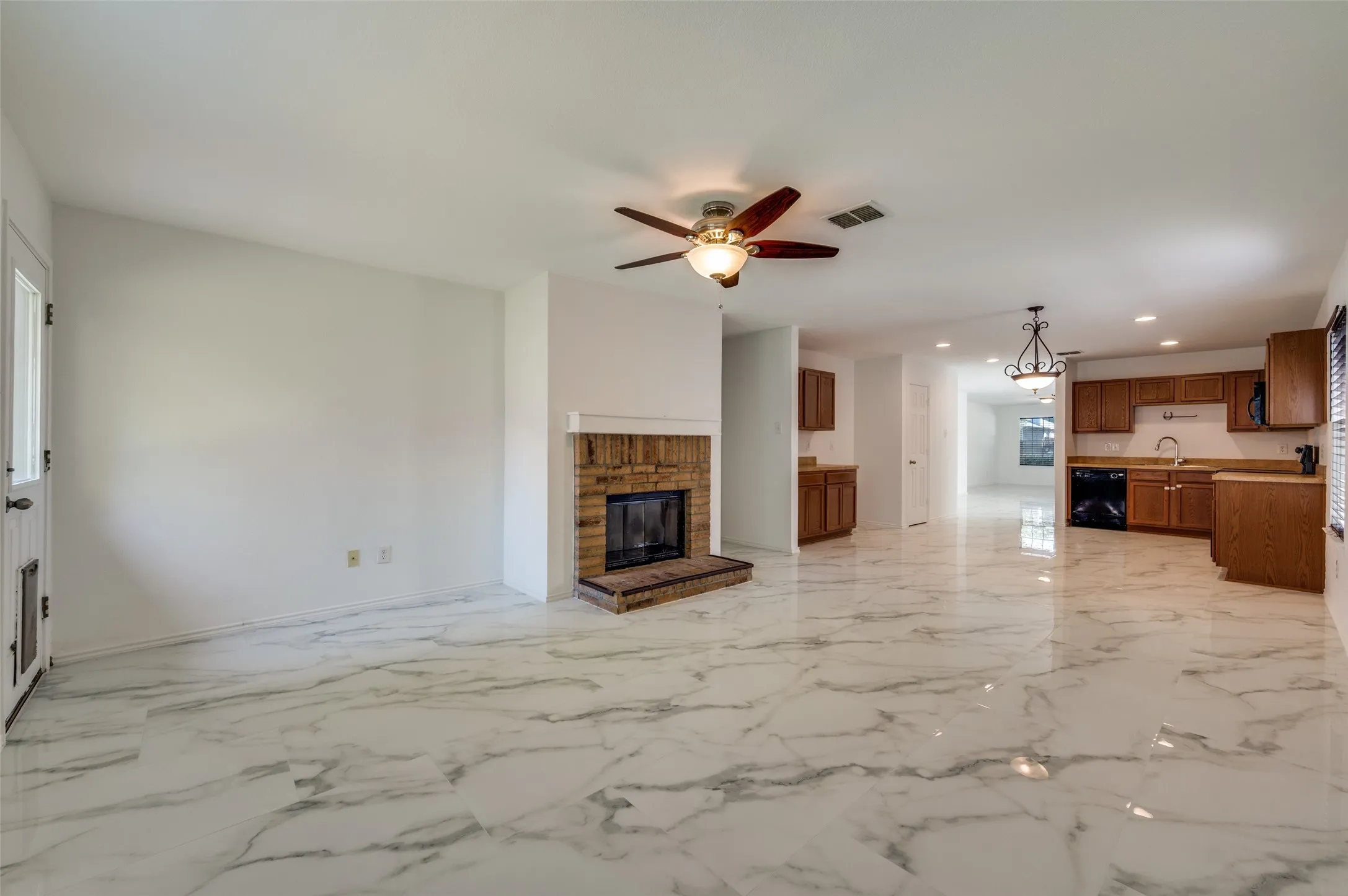 Open-concept living area with large-format marble-look tile flooring, a brick-surround fireplace with hearth, and a ceiling fan