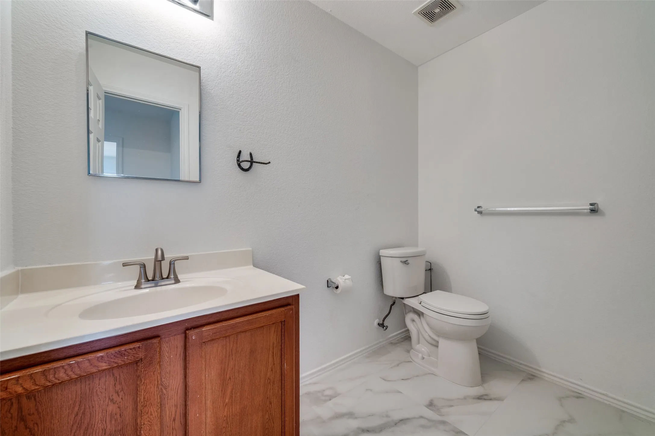 Bathroom featuring a wood-finish vanity with a light-toned countertop, a rectangular mirror, and marble-look floor tiling
