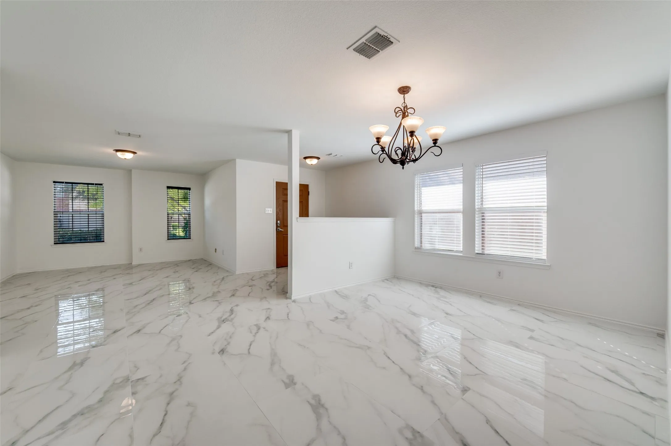 Open-concept interior featuring polished tile flooring with a marble-effect finish, a multi-light chandelier, and multiple windows with horizontal blinds