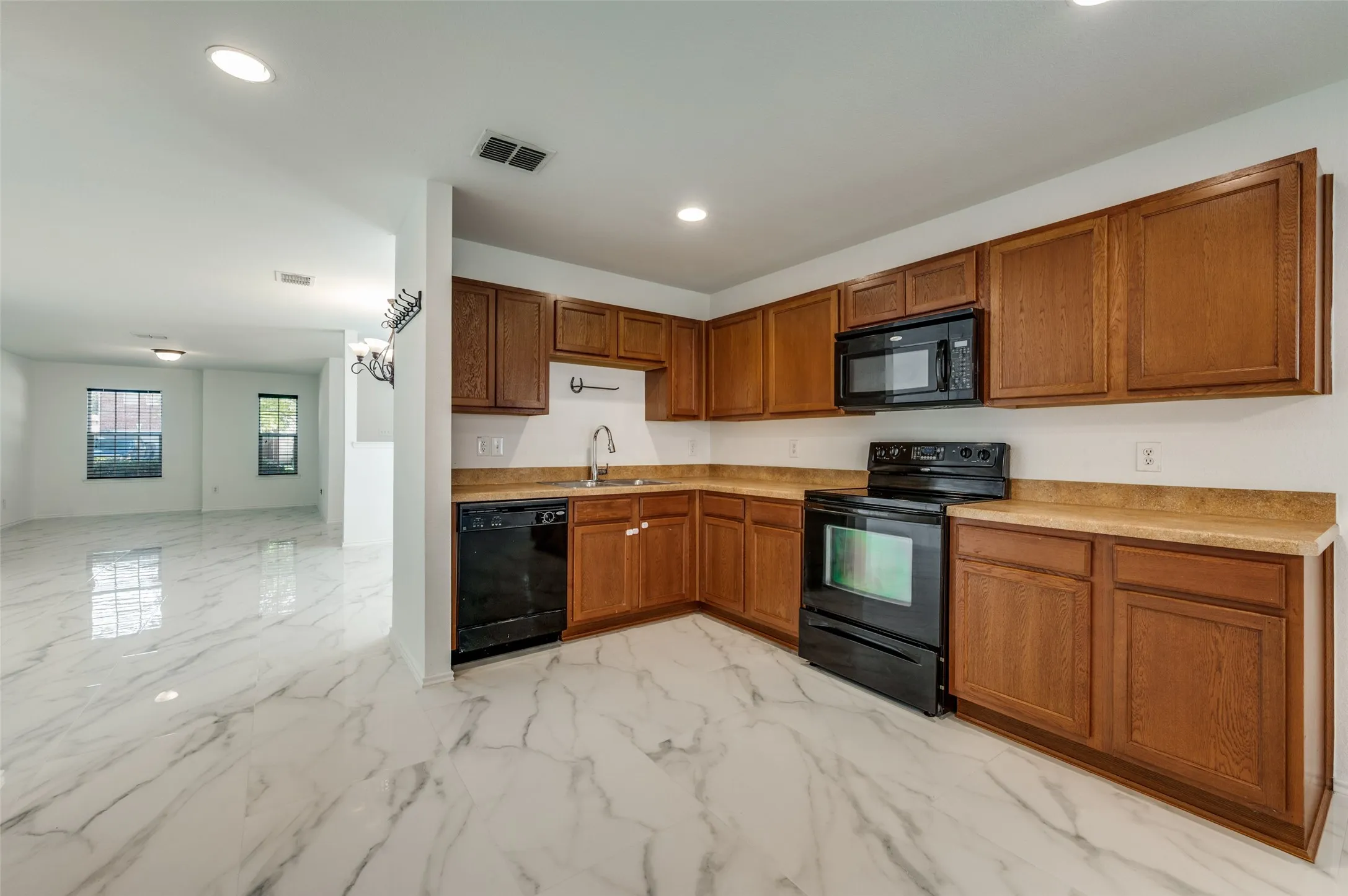 Kitchen featuring wood cabinetry, black appliances, light-toned countertops, and a white tile backsplash