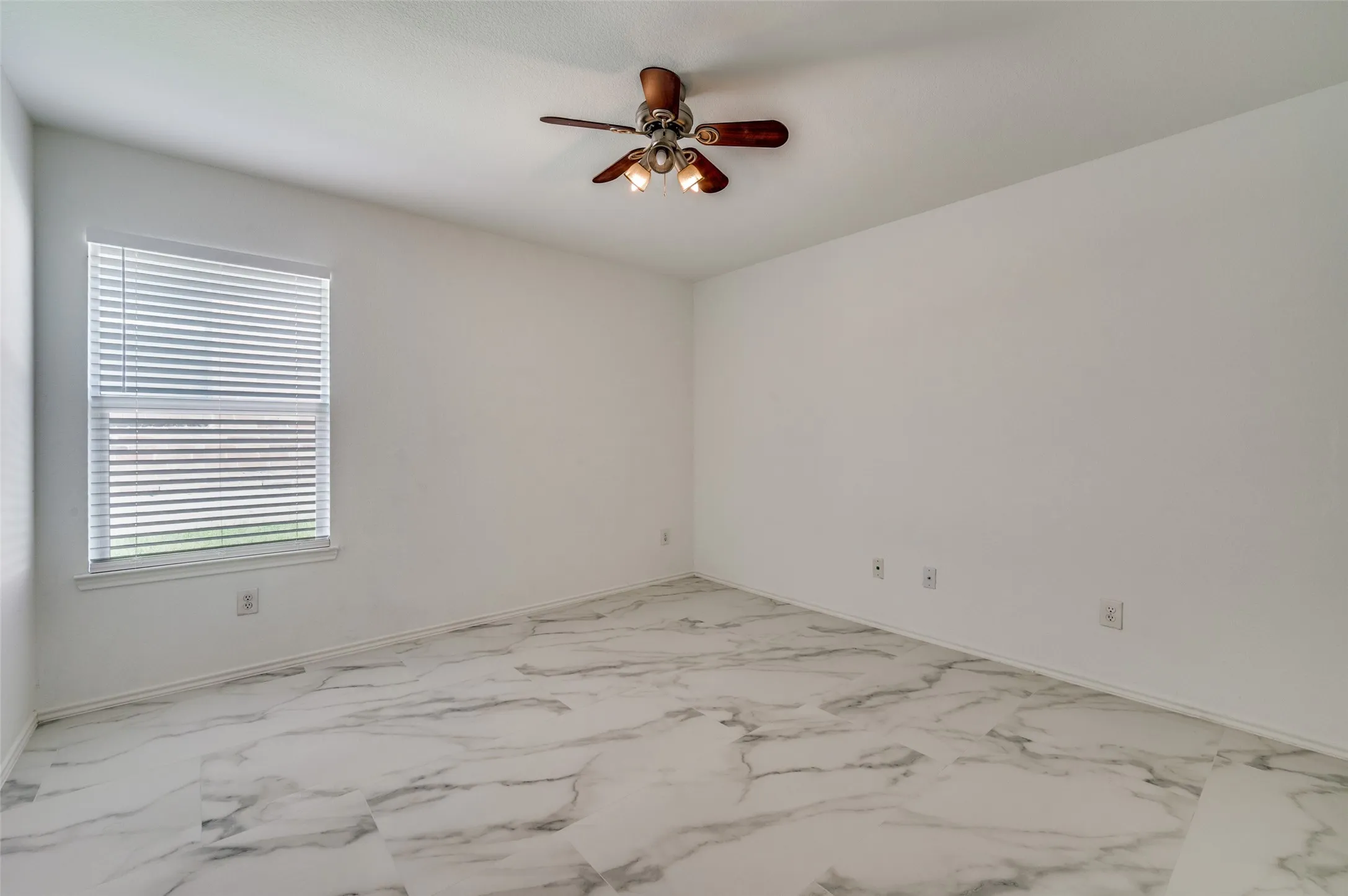 Spacious room featuring white walls, large window with blinds, and a wood-finish ceiling fan with integrated lighting