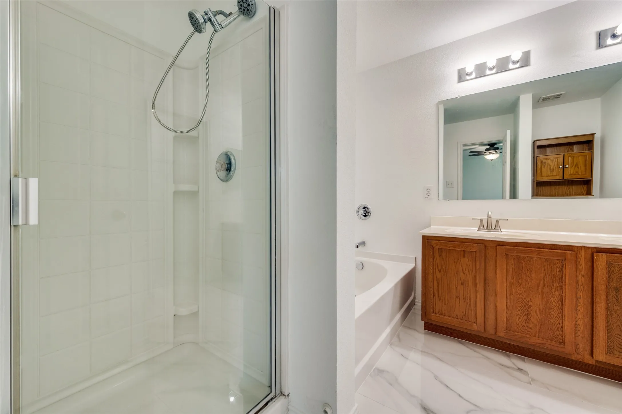 Bathroom featuring a glass-enclosed shower, an alcove bathtub, a long wood-finish vanity with ample storage, a large mirror, and marbling tile flooring