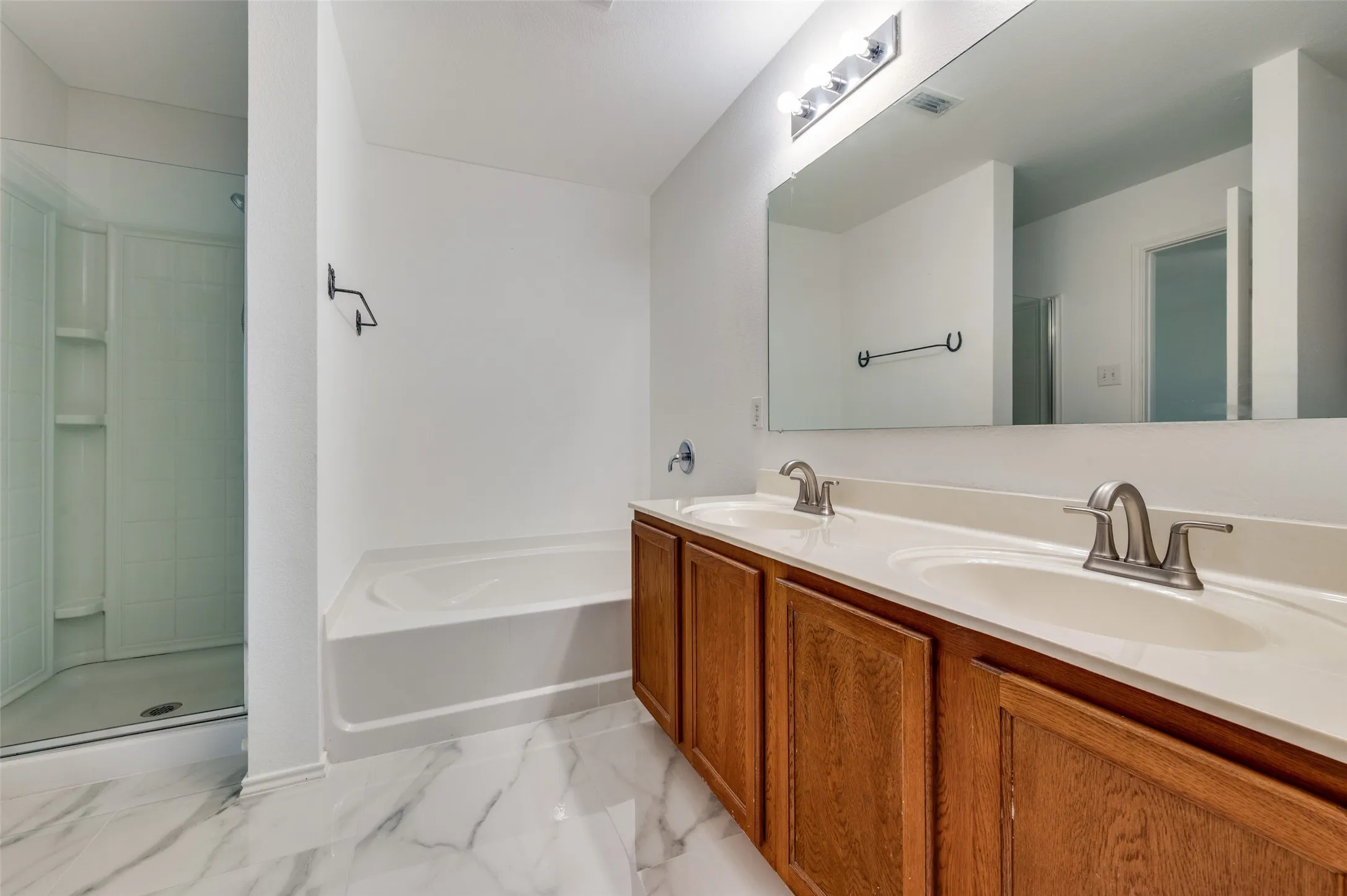 Spacious bathroom featuring a double vanity with wood cabinetry, brushed nickel fixtures, a large integrated mirror, a separate shower enclosure, and a built-in tub