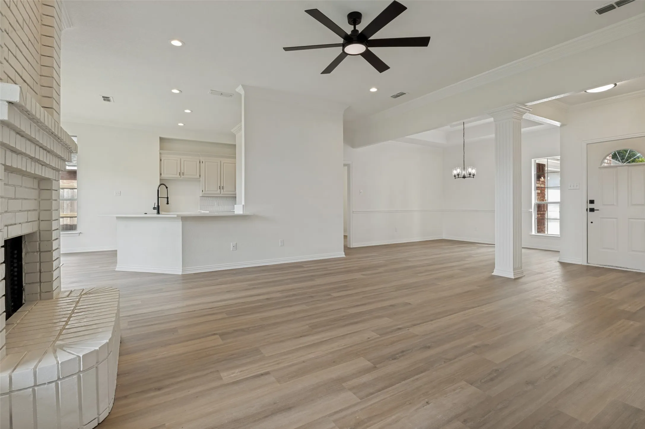 Expansive living area with light wood-finish flooring and a white brick fireplace