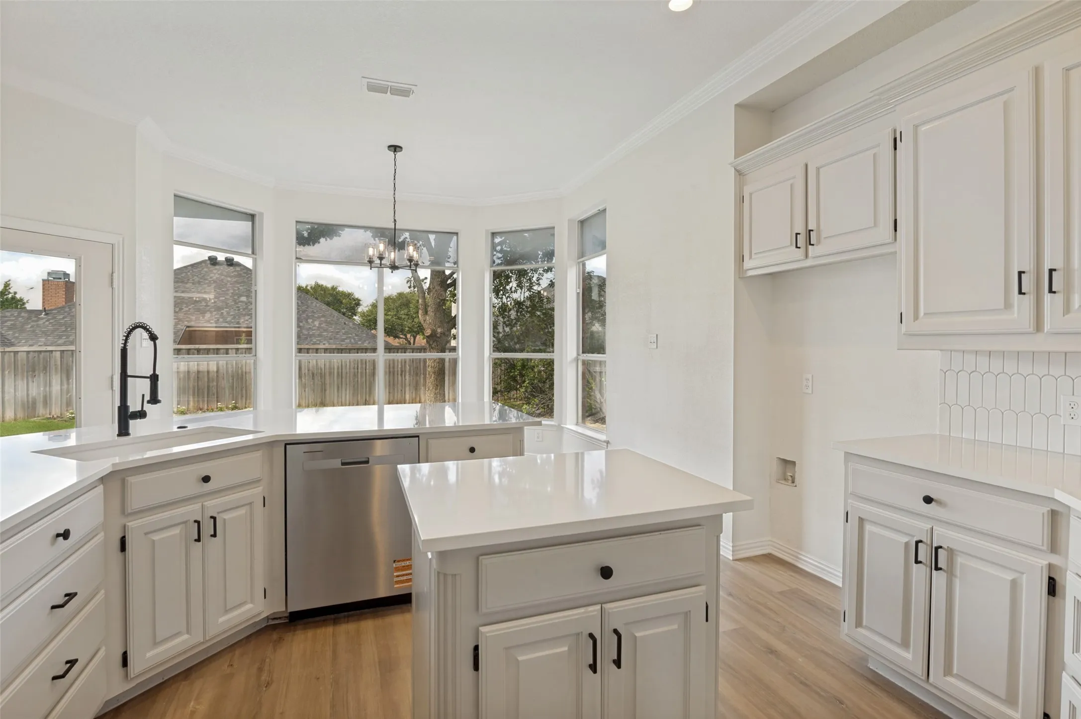 Bright kitchen featuring white cabinetry, quartz countertops, stainless steel dishwasher, modern black faucet, and a decorative chandelier