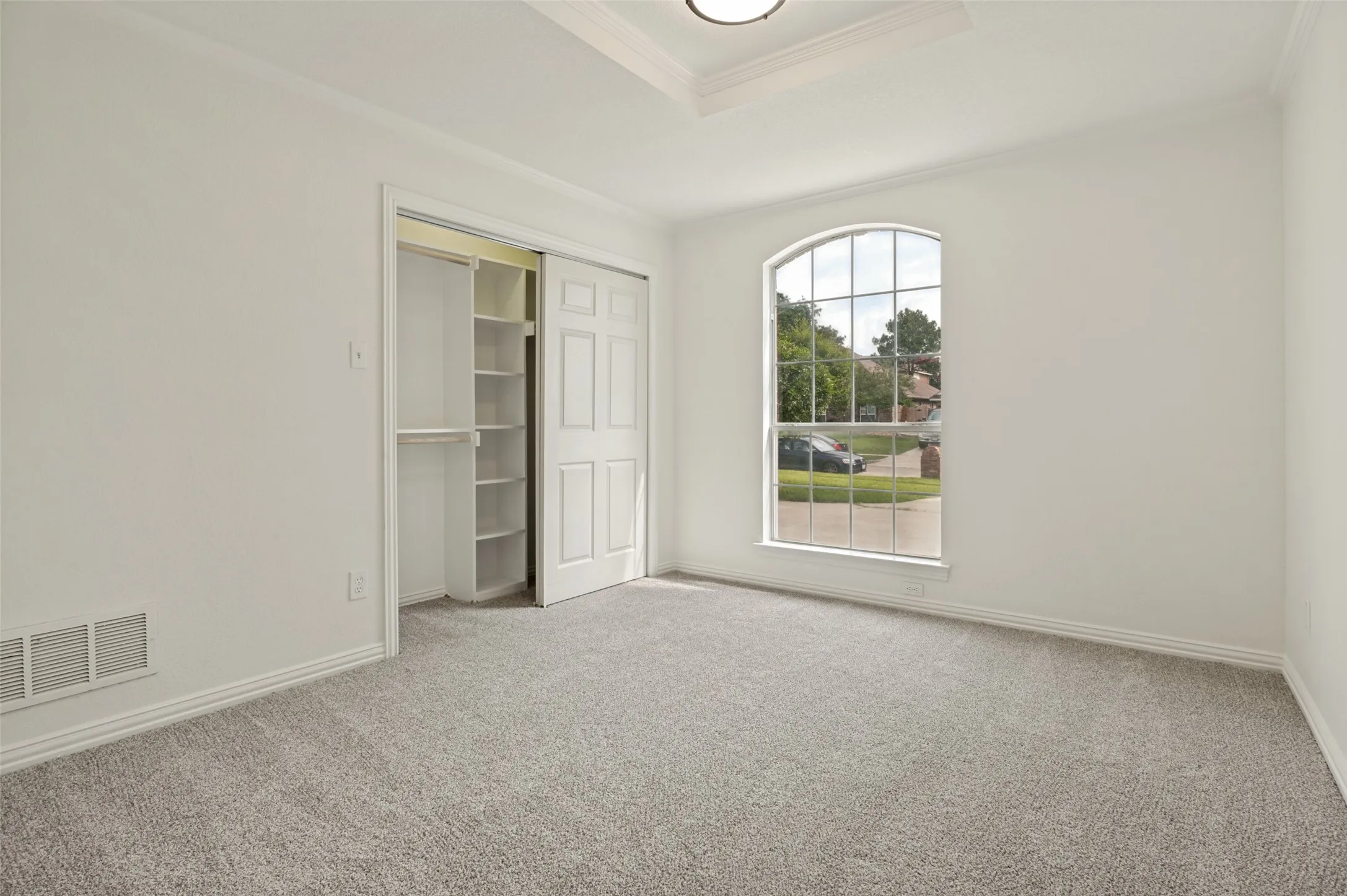 Room featuring an arched window, white trim, and light gray carpet