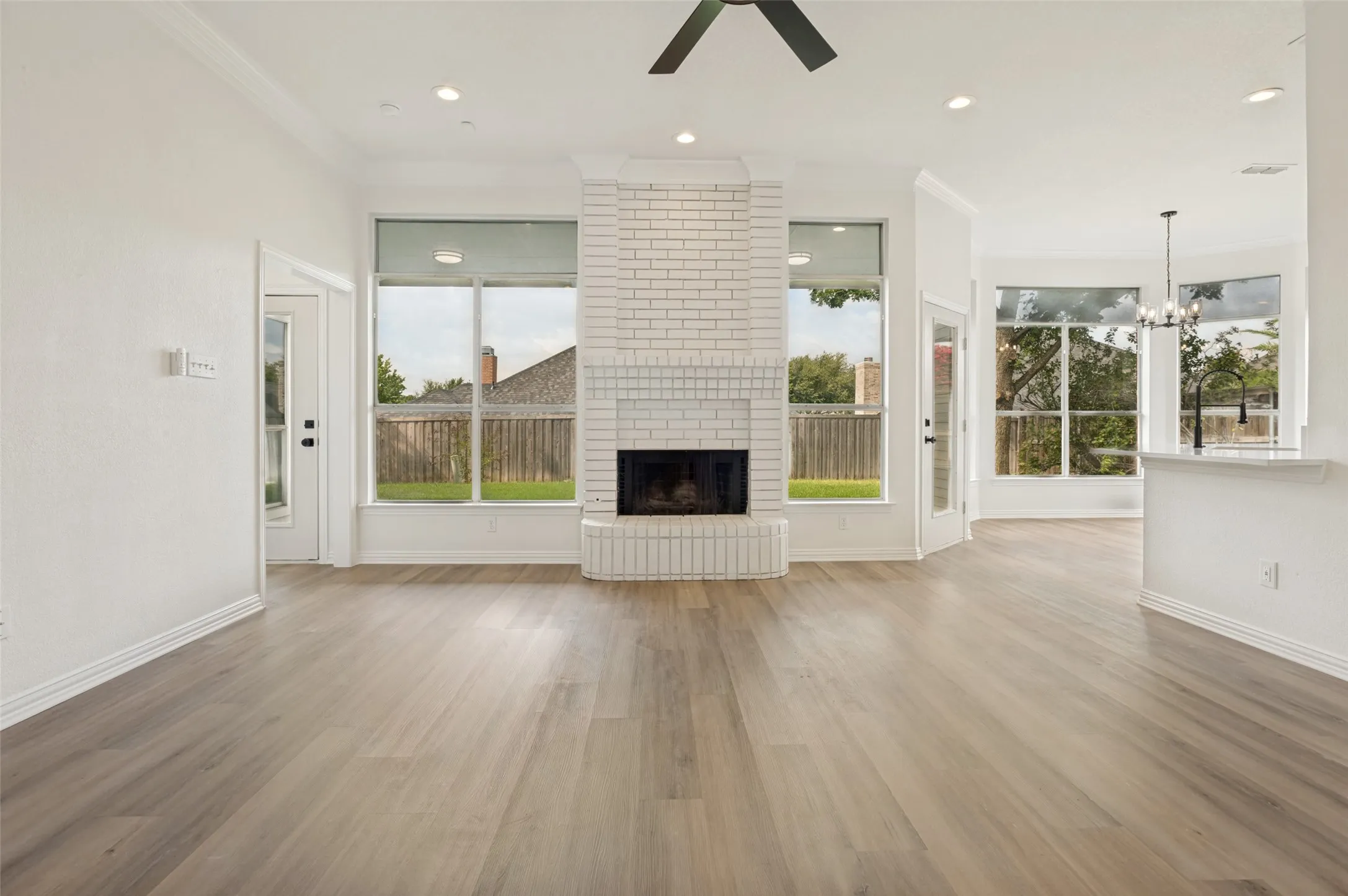 Expansive living area with wood-finish flooring, a white brick fireplace, recessed lighting, and multiple large windows