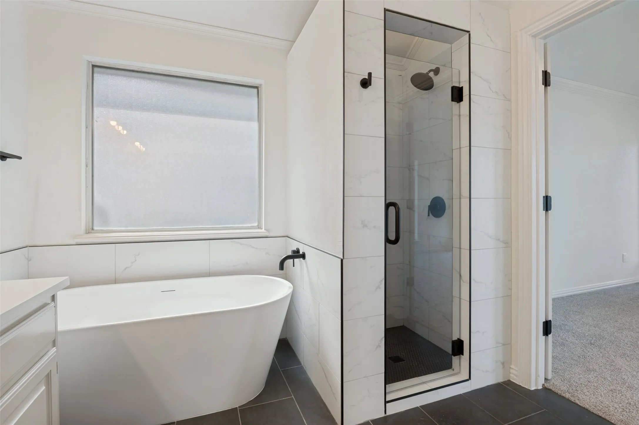 Contemporary bathroom featuring a freestanding soaking tub, a frameless glass shower enclosure with matte black fixtures, and large format tile flooring