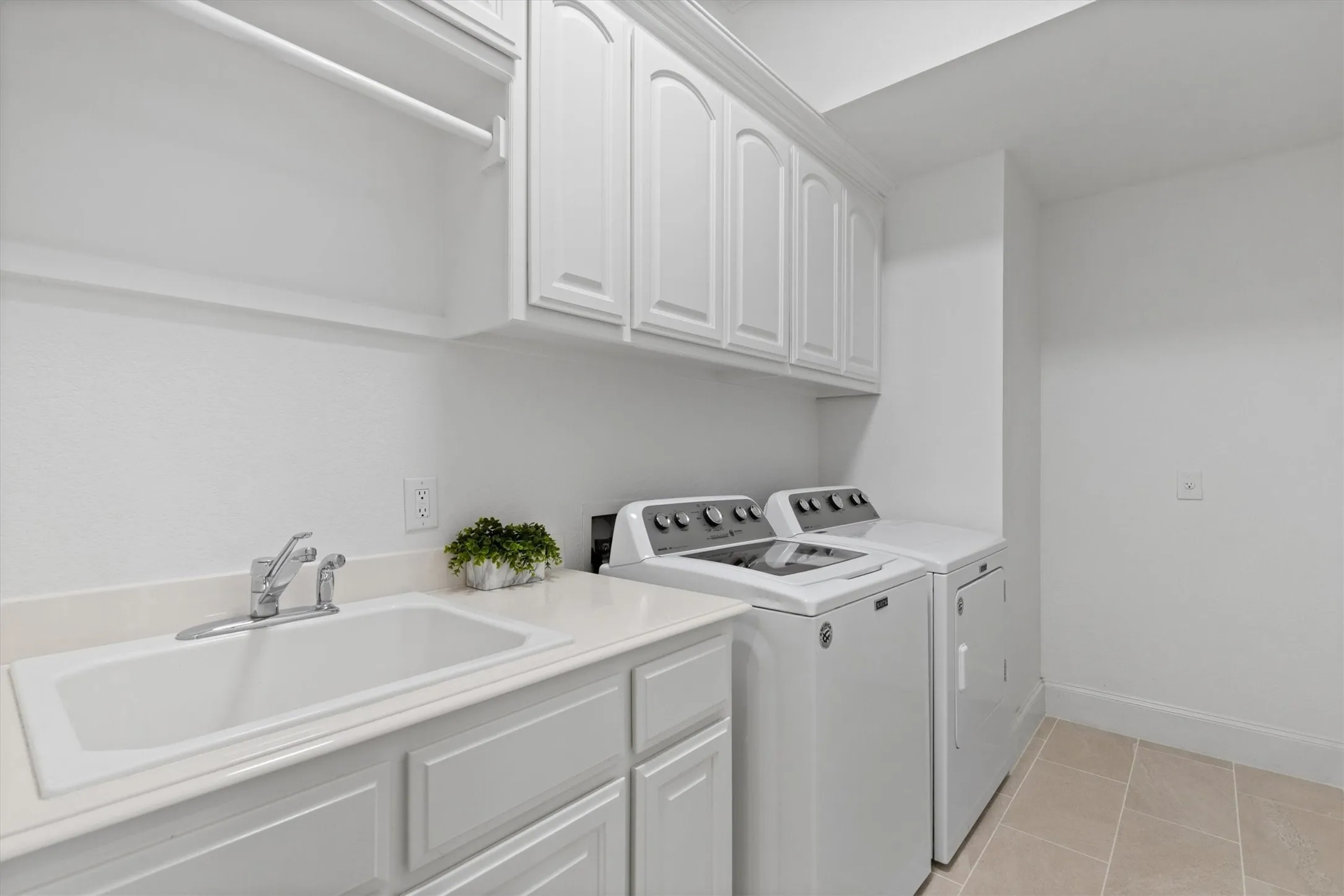 Dedicated laundry room featuring a utility sink, white cabinetry, a built-in hanging rod, light-toned tiled flooring, and a stone-finish countertop