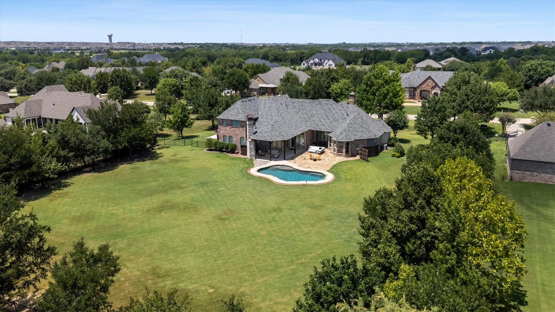 Expansive property featuring a large manicured lawn, a freeform swimming pool, and a brick exterior home with a grey shingle roof