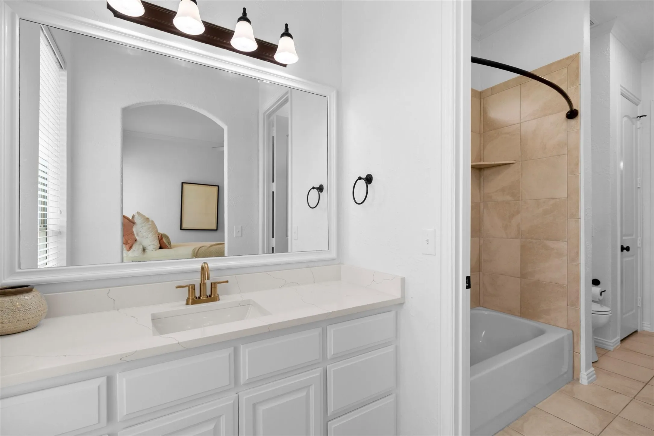 Bathroom vanity with white cabinetry, a light-colored countertop, and a rectangular undermount sink with a brass-finish faucet