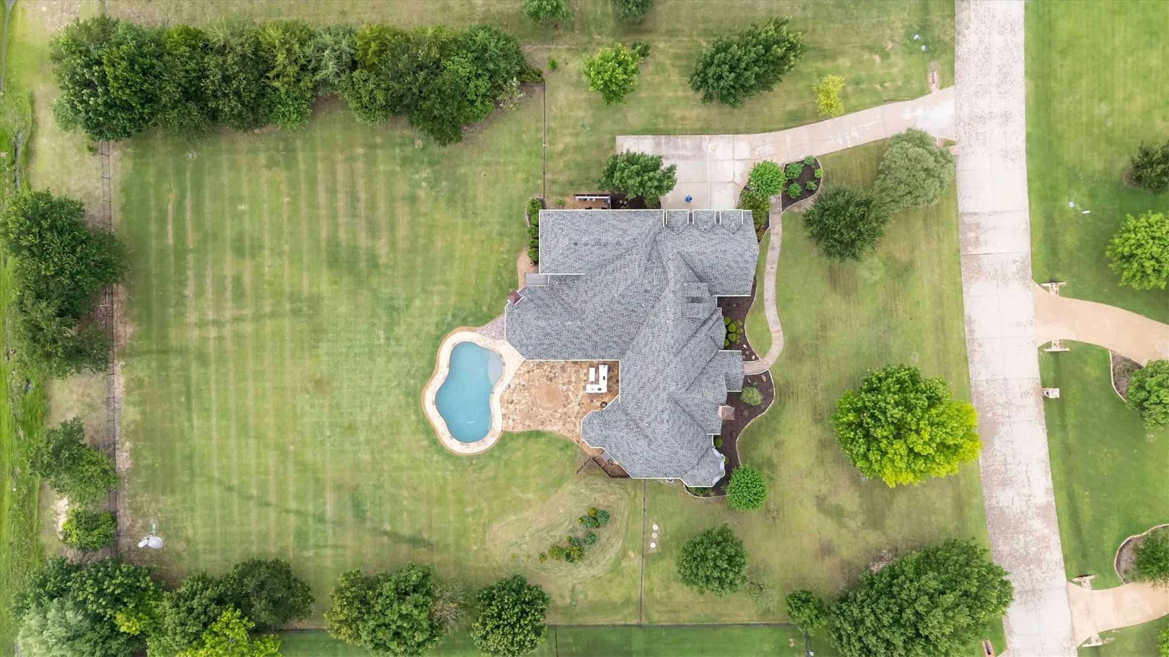 Expansive property featuring a large backyard, freeform swimming pool, concrete patio, and a shingle roof