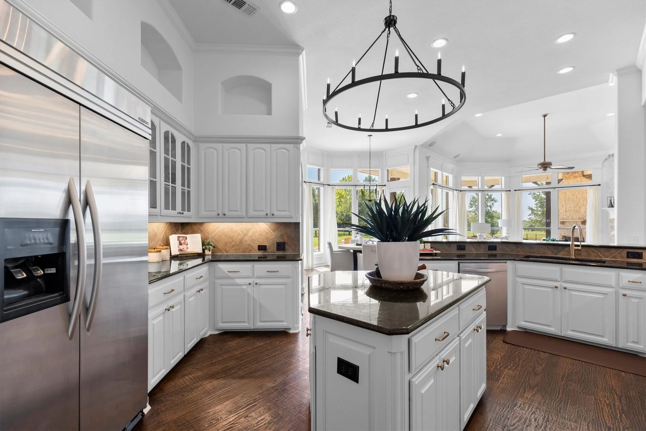 Spacious kitchen featuring white cabinetry, dark stone countertops, stainless steel appliances, dark wood-finish flooring, and a large central island