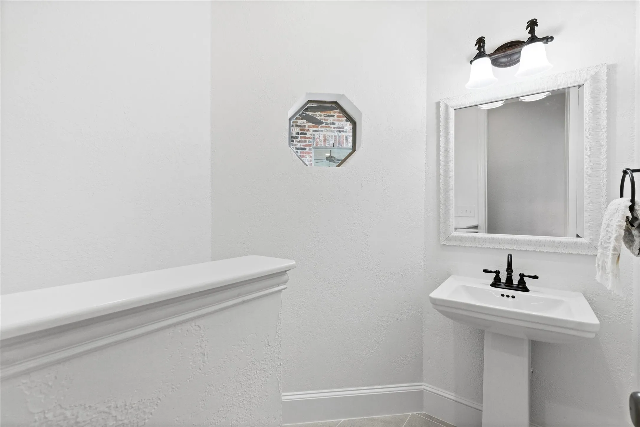 Pedestal sink with matte black faucet, wall-mounted mirror, and overhead vanity lighting