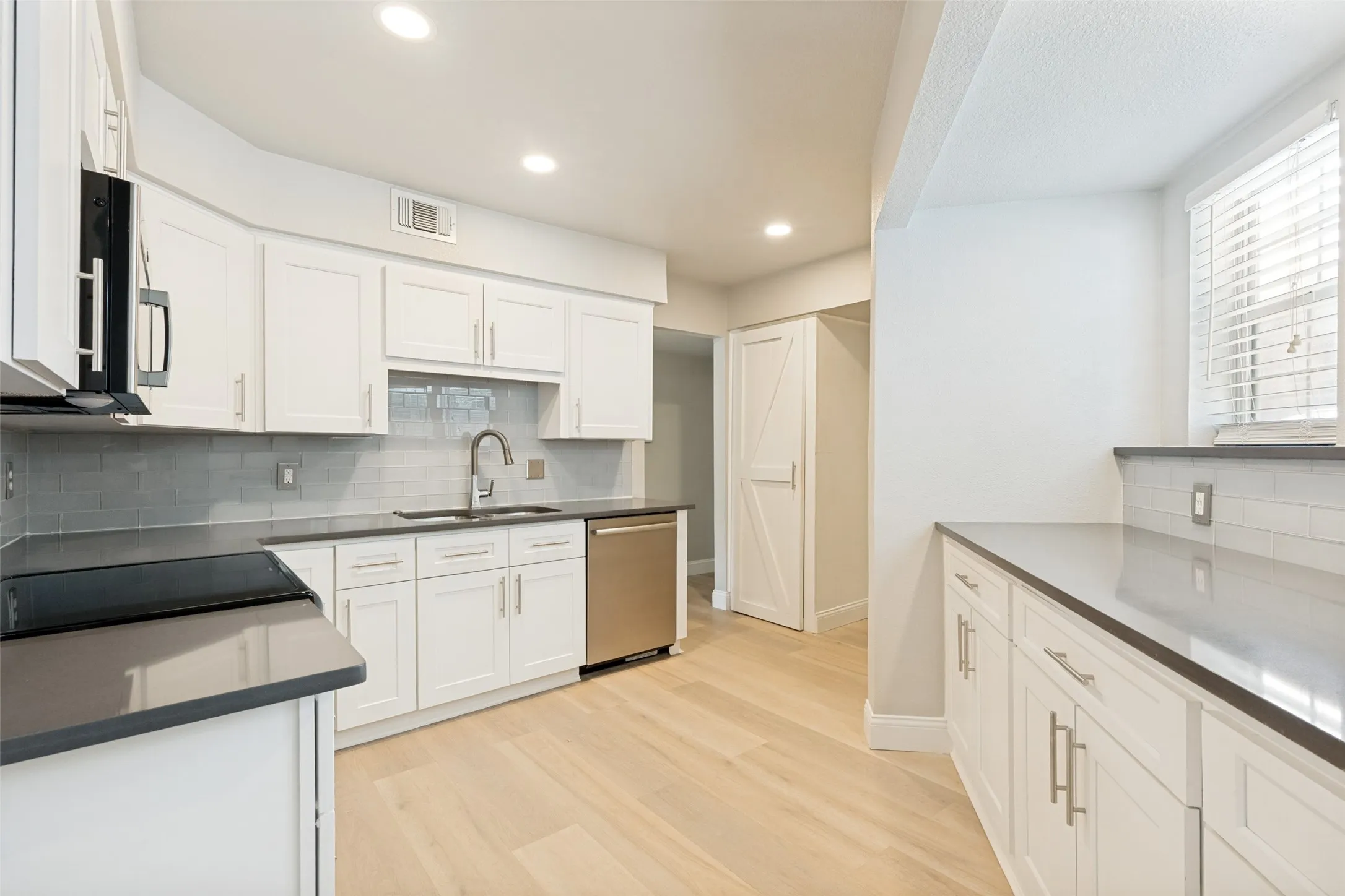 Renovated kitchen featuring light wood-finish flooring, white cabinetry with brushed nickel hardware, stainless steel appliances, a tile backsplash, and recessed lighting