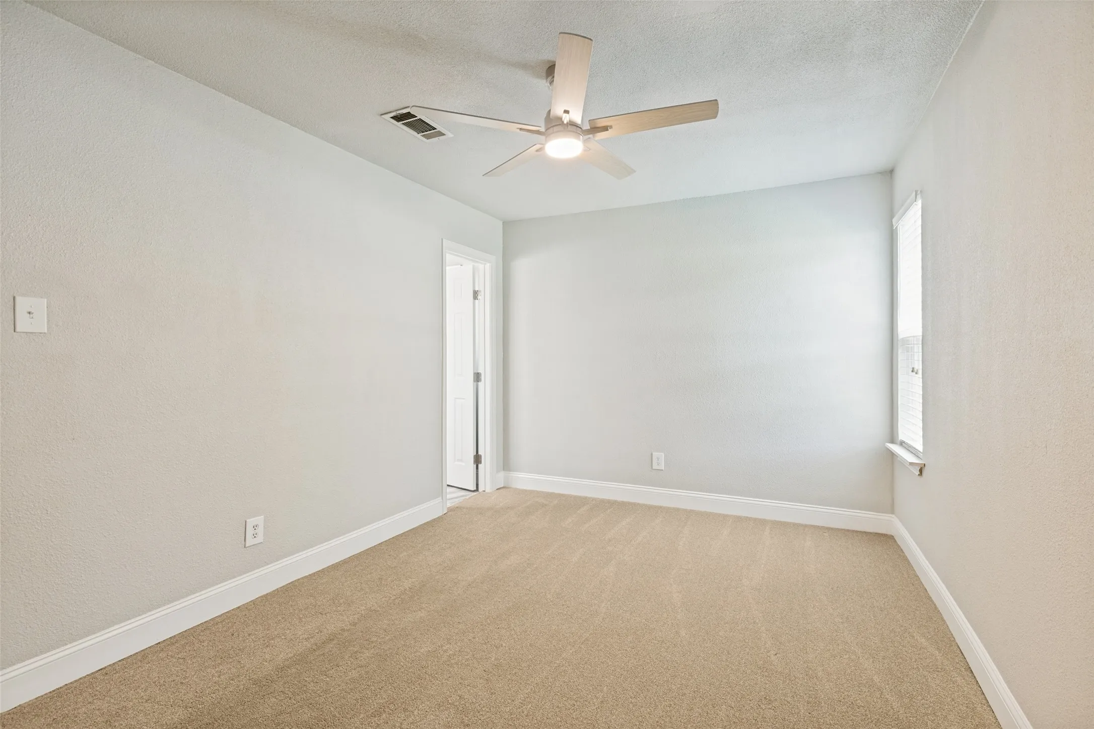 Neutral-toned carpeting and light-colored walls define this room, featuring a ceiling fan with integrated lighting