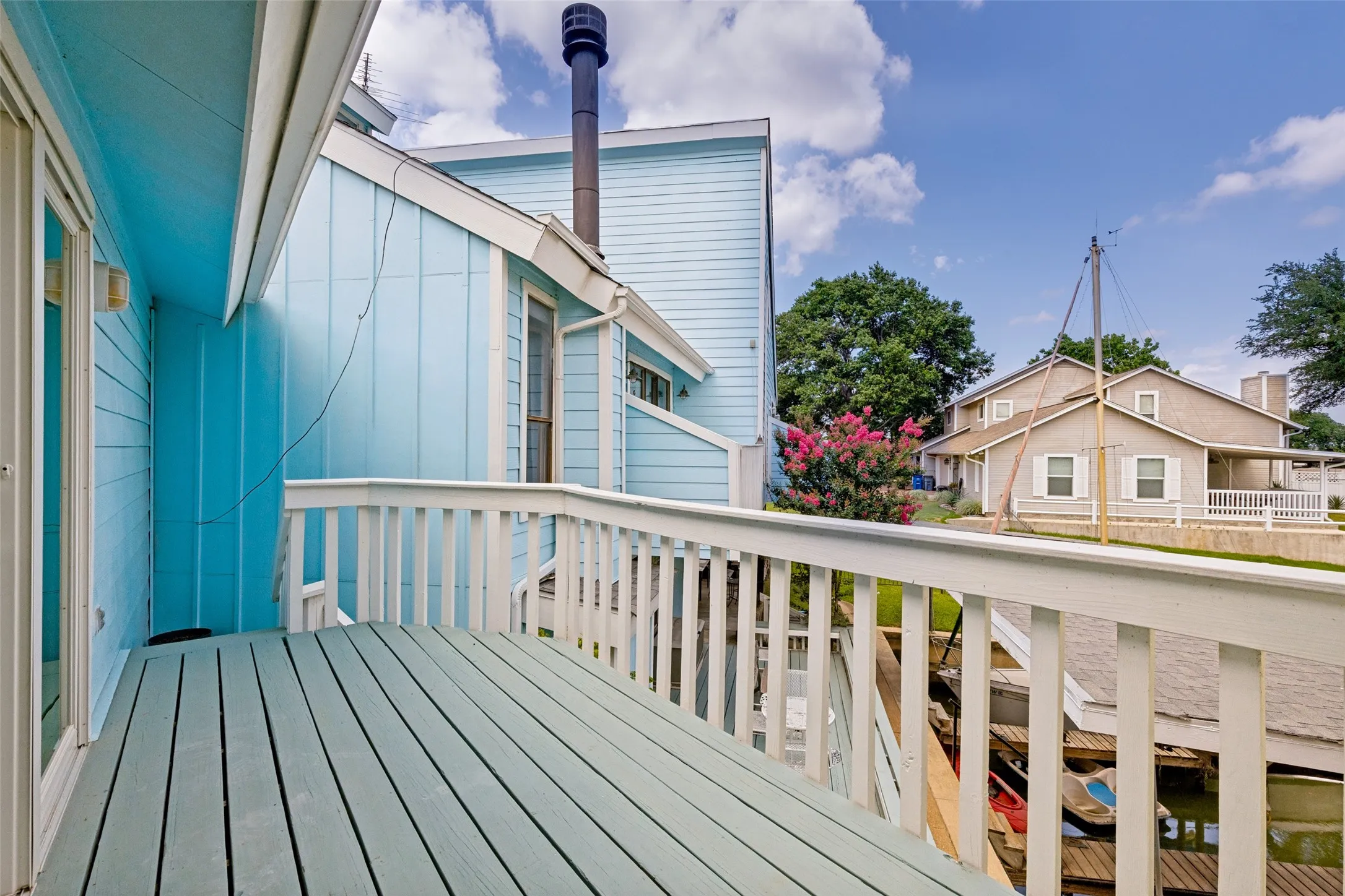 Wooden deck with white railing, featuring a light blue exterior siding and a sliding glass door