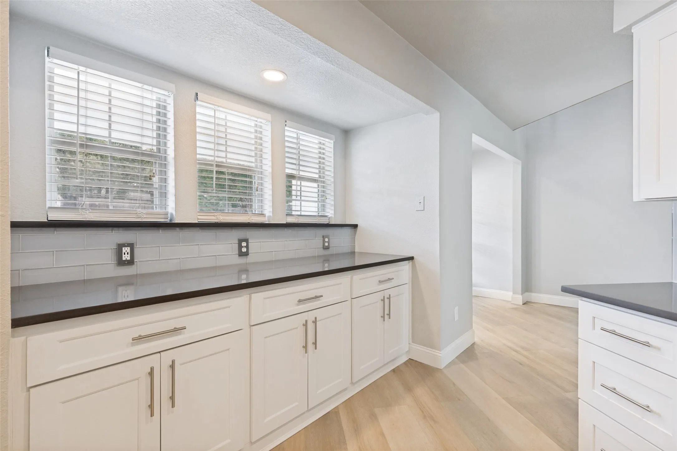 Kitchen featuring dark countertops, light gray subway tile backsplash, white shaker cabinetry, recessed lighting, and wood-finish flooring
