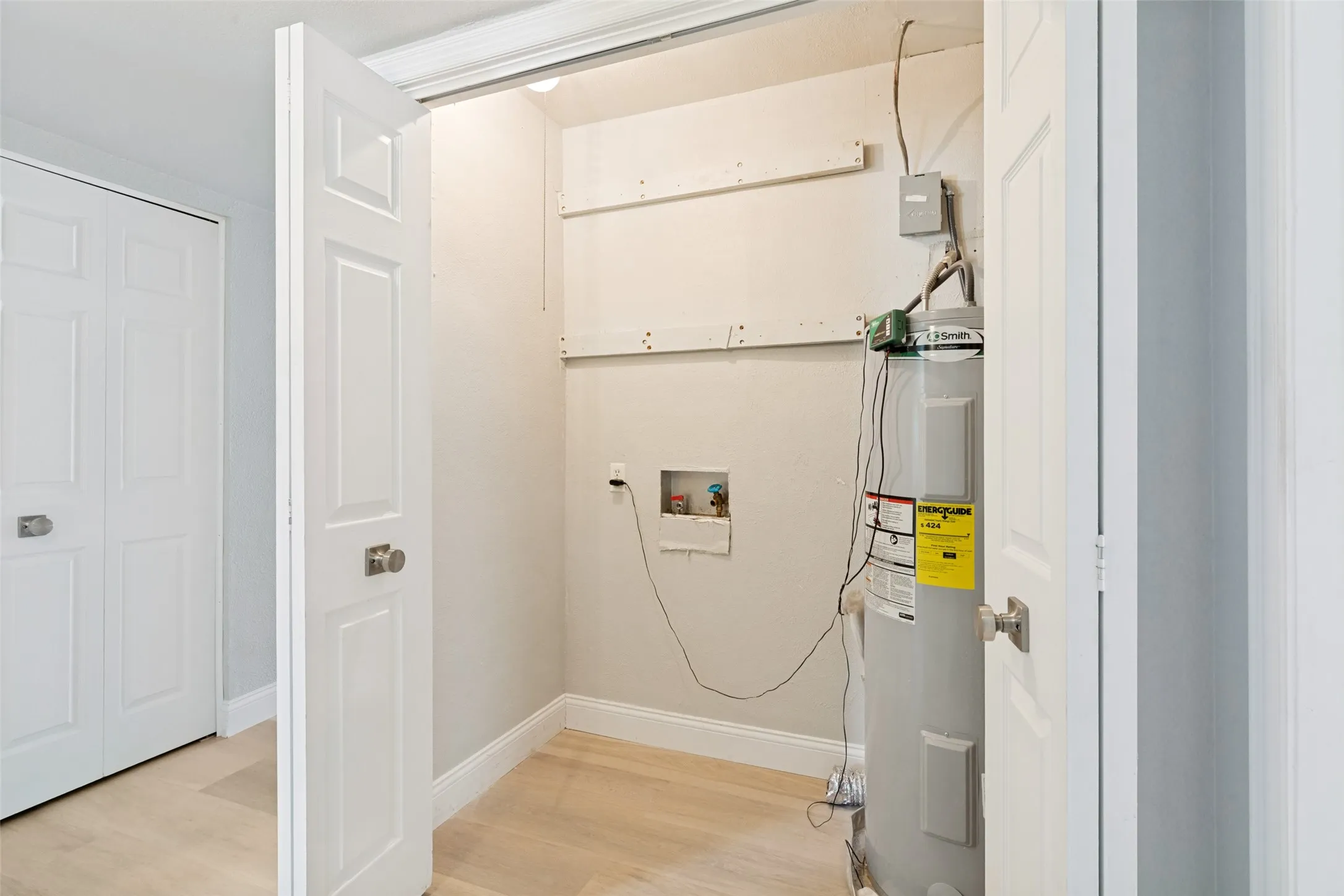 Utility closet featuring a water heater, washer/dryer hookups, and wood-finish flooring