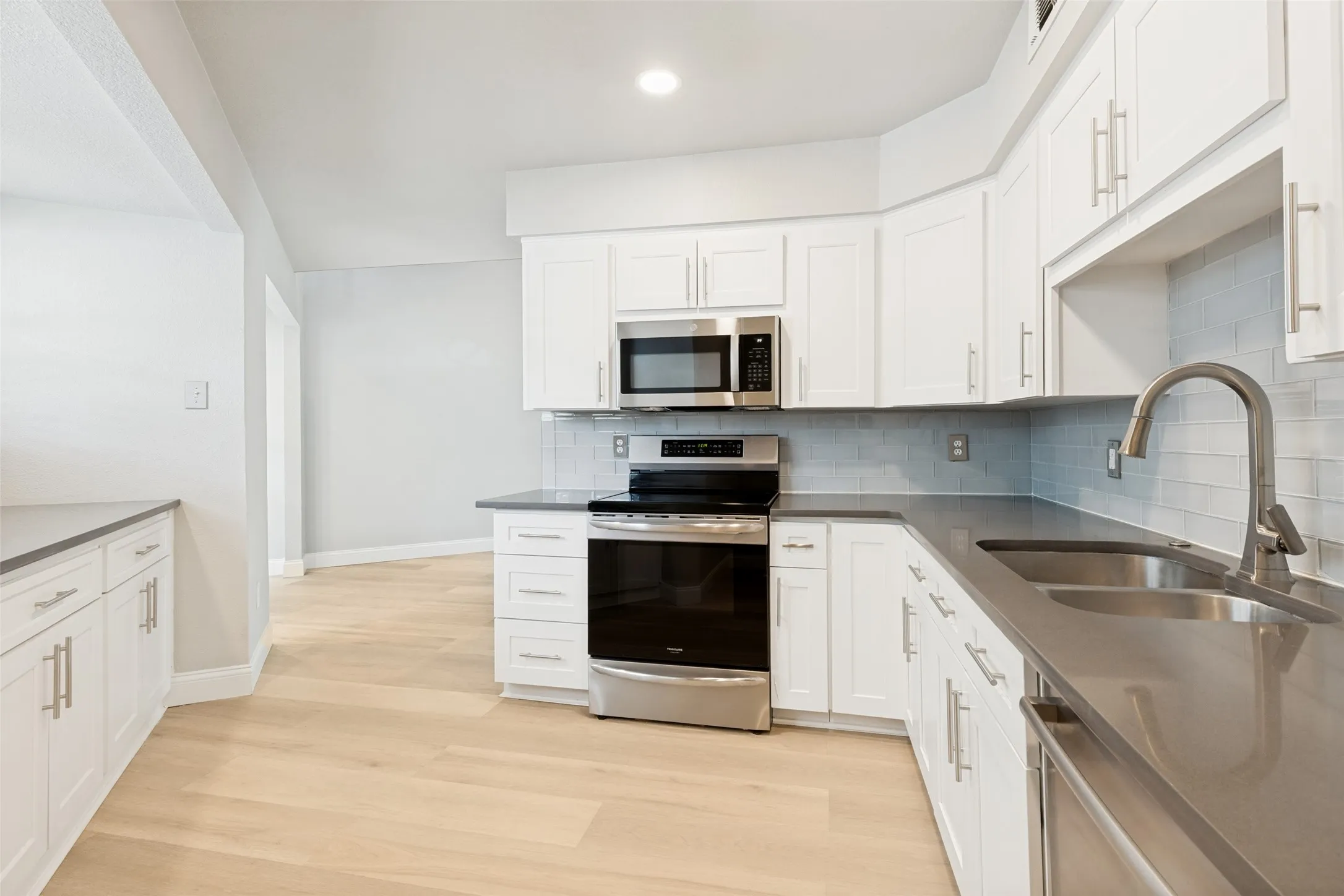 Contemporary kitchen featuring white cabinetry, stainless steel appliances, a subway tile backsplash, dark countertops, and light wood-finish flooring