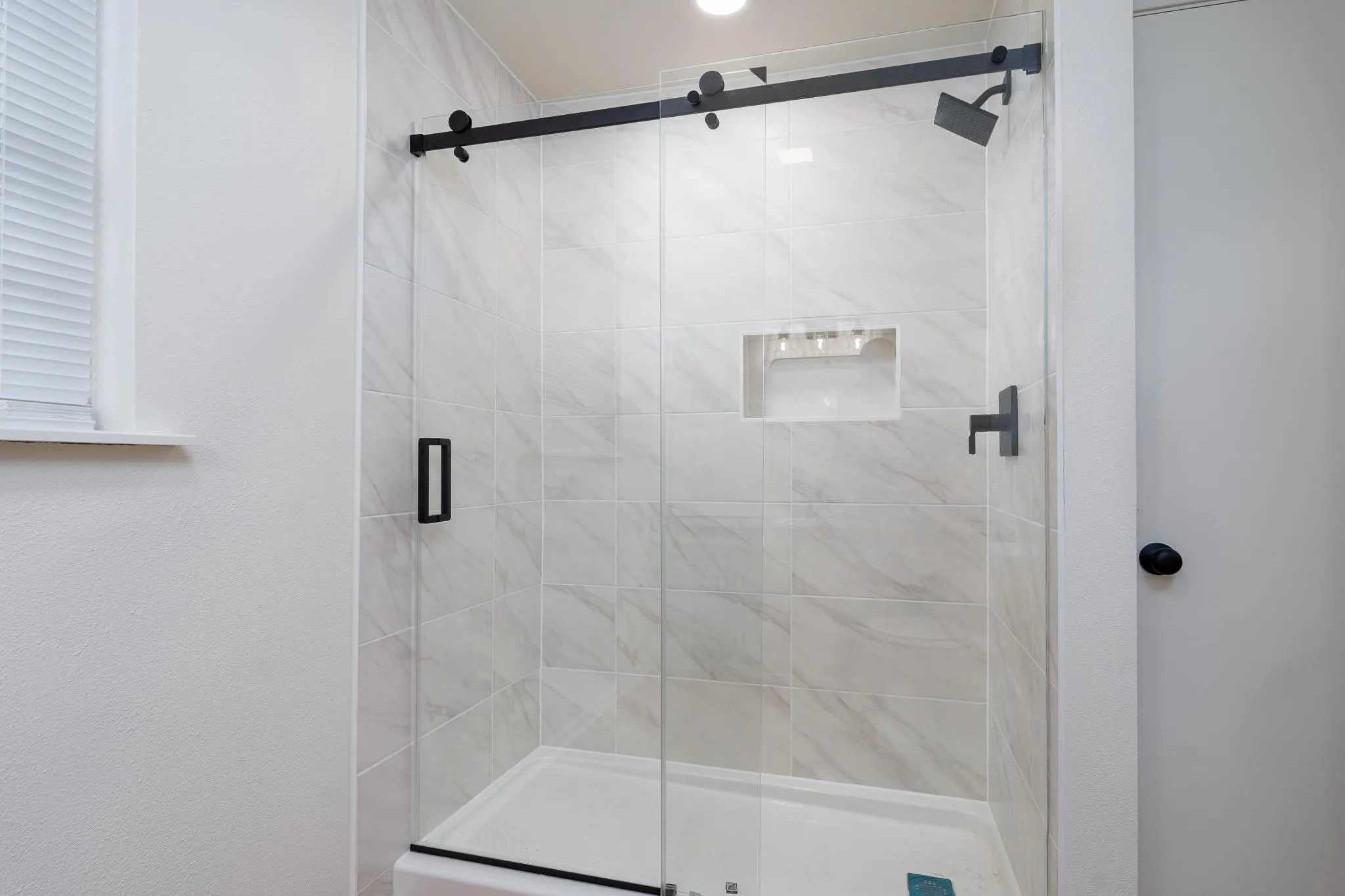 Shower enclosure with sliding glass door, tiled walls, built-in shower niche, and matte black fixtures