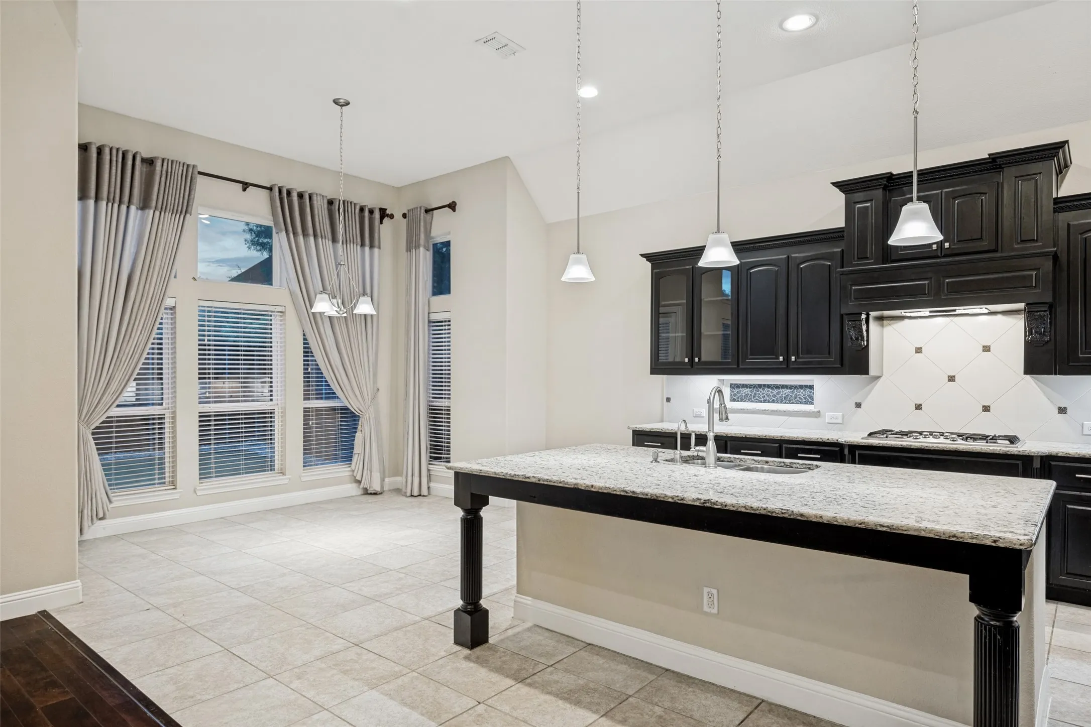 Open-concept kitchen with dark wood cabinetry, granite countertops, an island with a built-in sink, and tile flooring