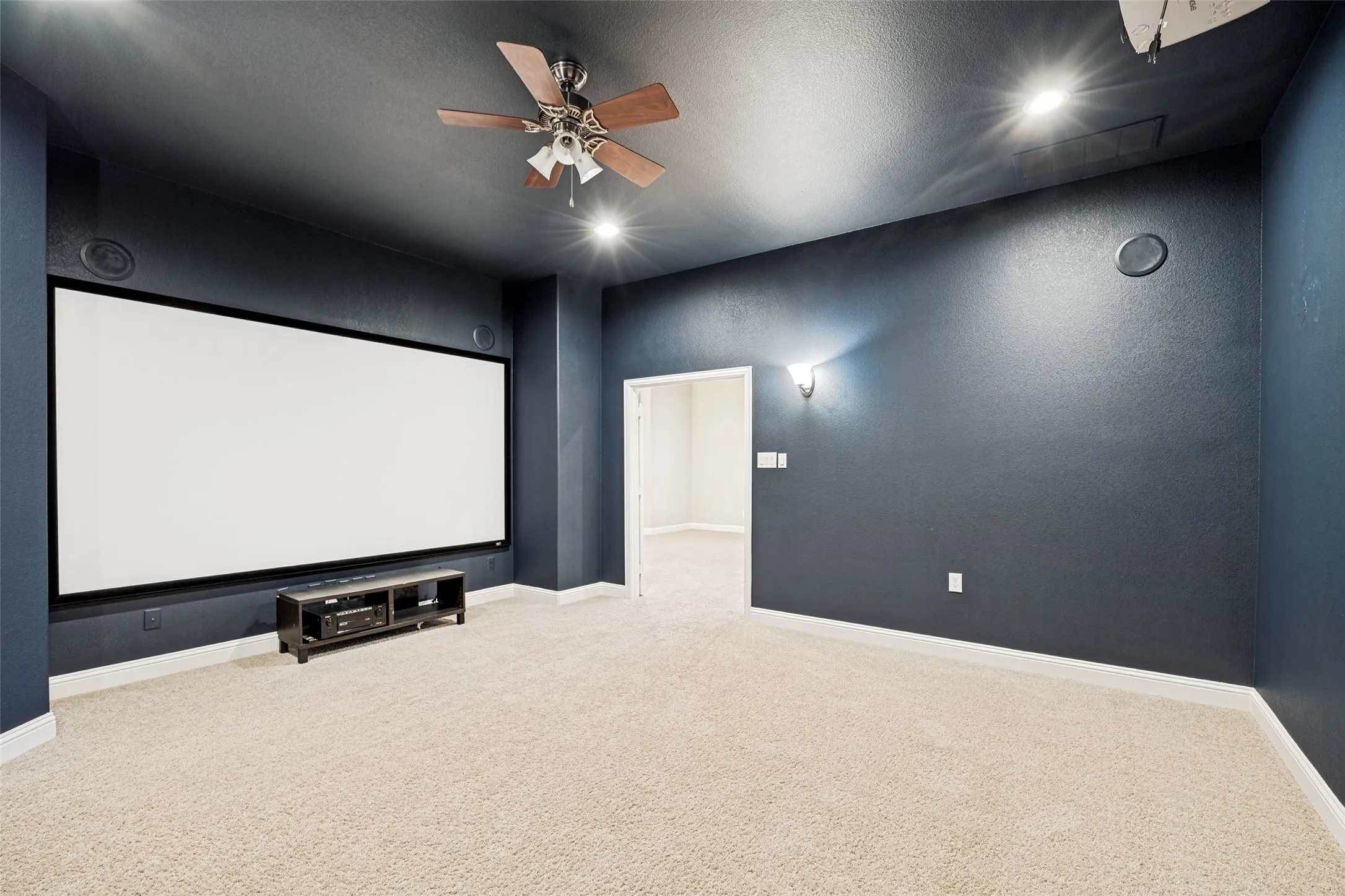 Dedicated media room featuring a large projection screen, recessed ceiling lighting, and a ceiling fan