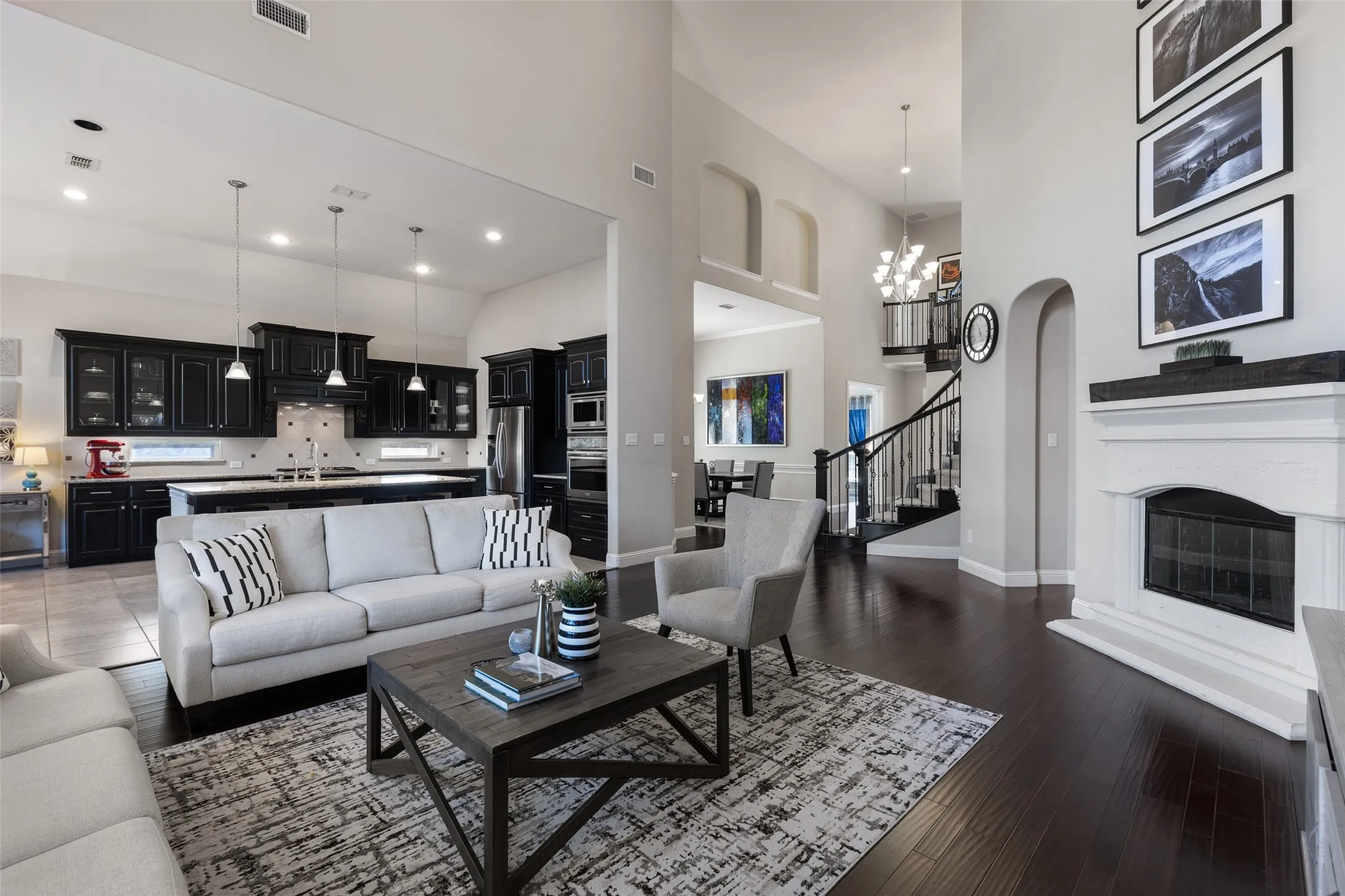 Spacious open-concept living area featuring dark wood-finish flooring, a white mantel fireplace, and a two-story ceiling