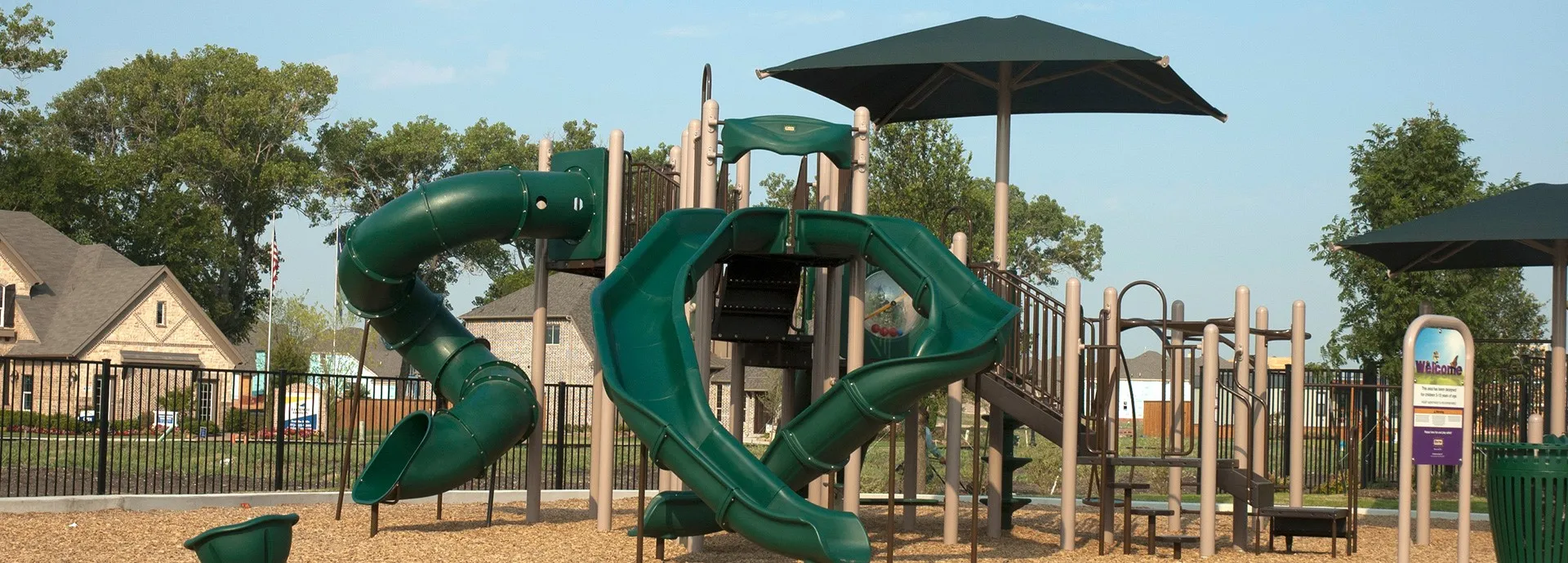 Community playground featuring multiple slides, climbing structures, and shade canopies over wood chip surfacing