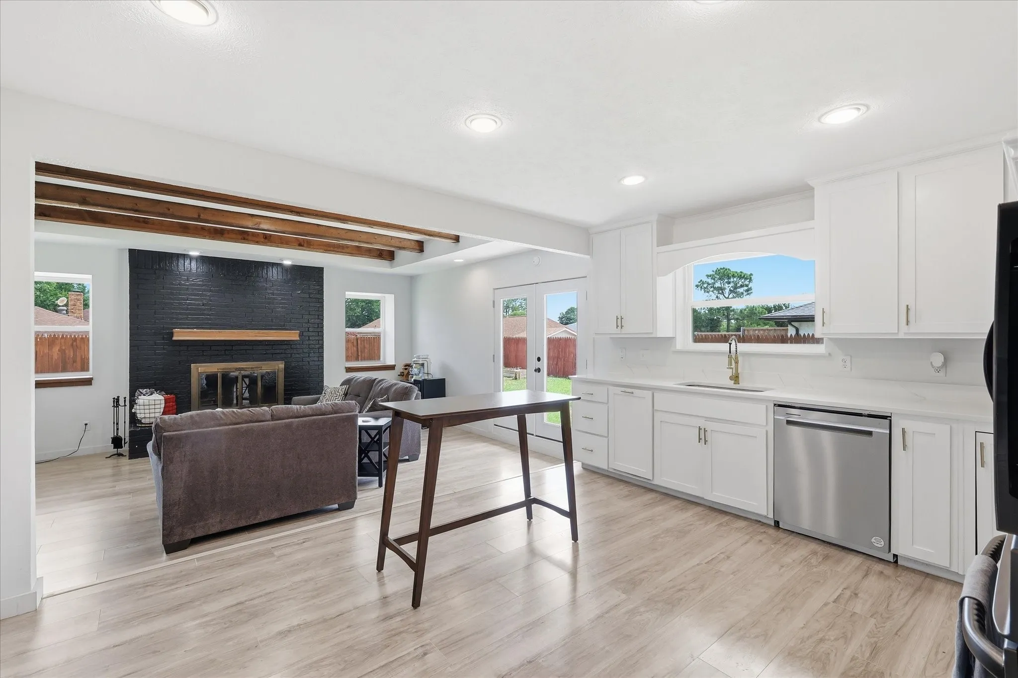 Open-concept living space featuring wood-finish flooring, recessed lighting, and a kitchen with white cabinetry, a stainless steel dishwasher, and a window above the sink