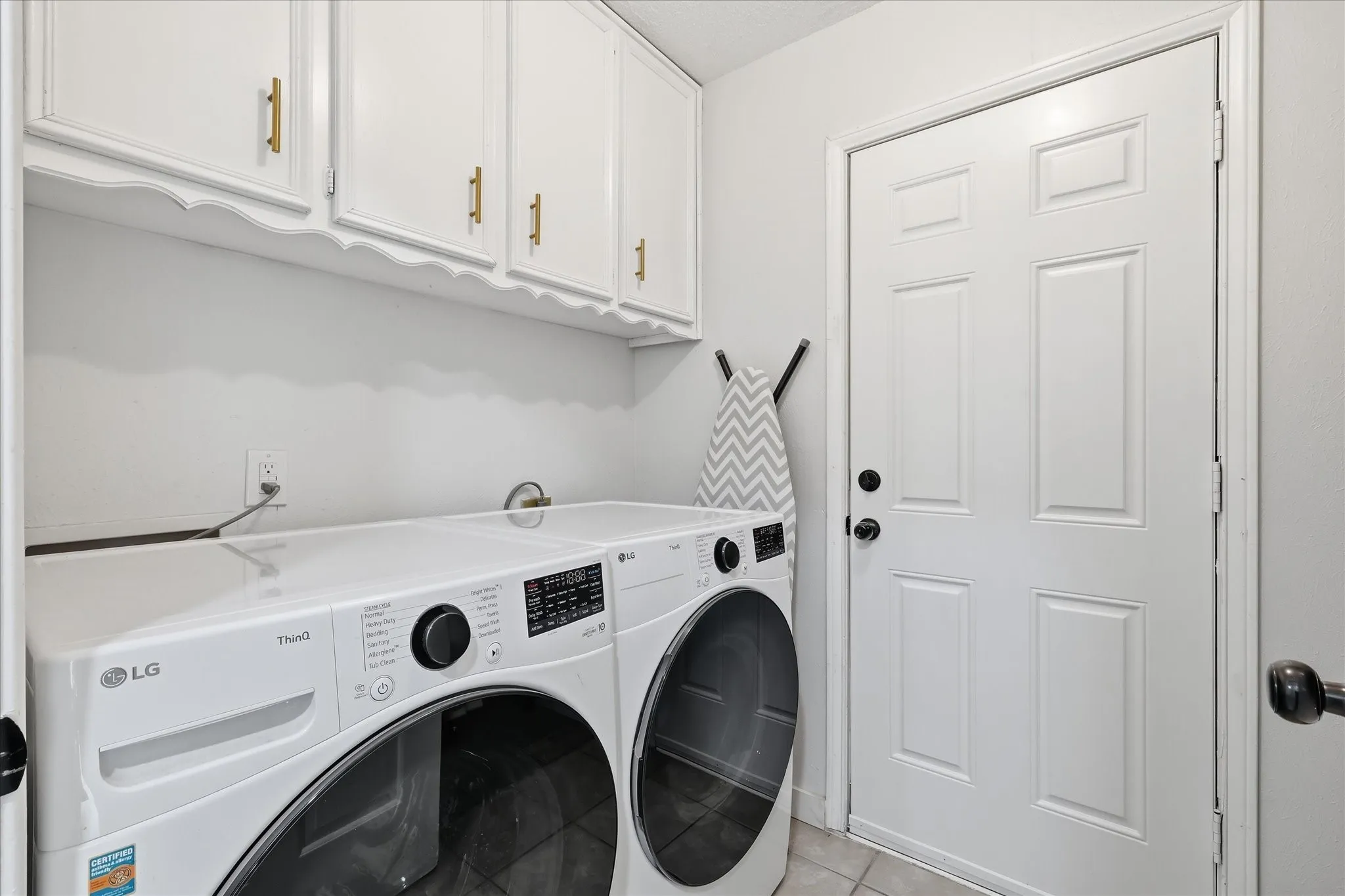Laundry area featuring white cabinetry with gold-finish hardware, a paneled door with black hardware, and tiled flooring