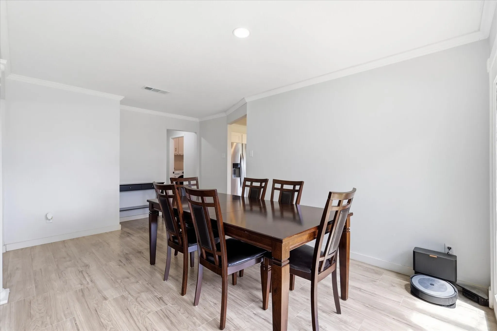 Spacious room featuring light wood-finish flooring, crisp white crown molding, recessed lighting, and bright white walls