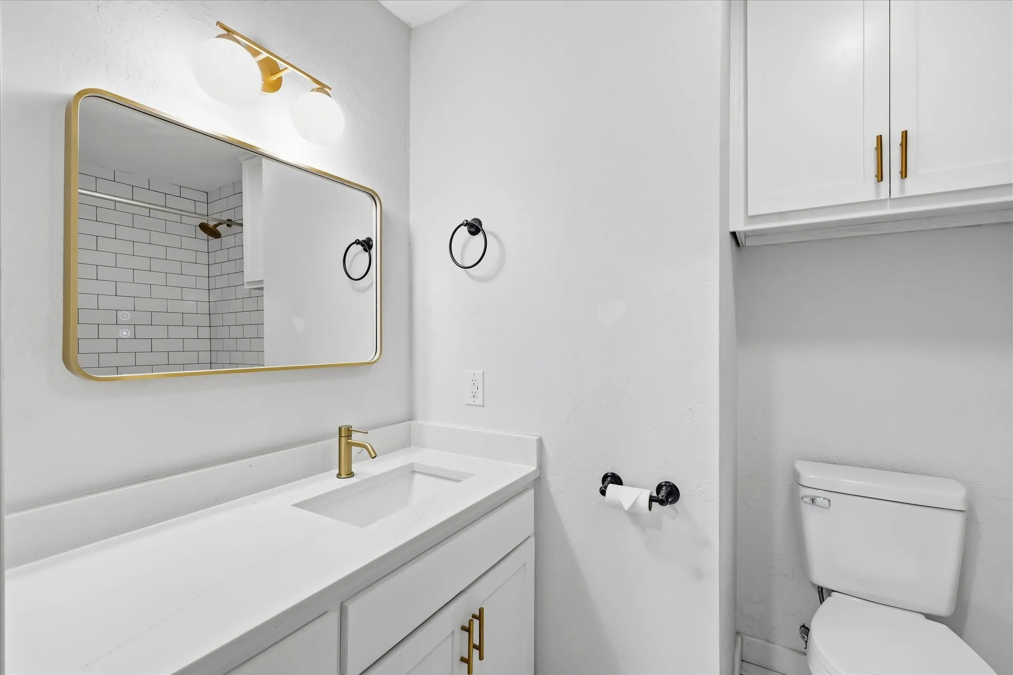 Bathroom featuring a white vanity with an integrated sink, gold-finish faucet, and coordinating gold-framed mirror