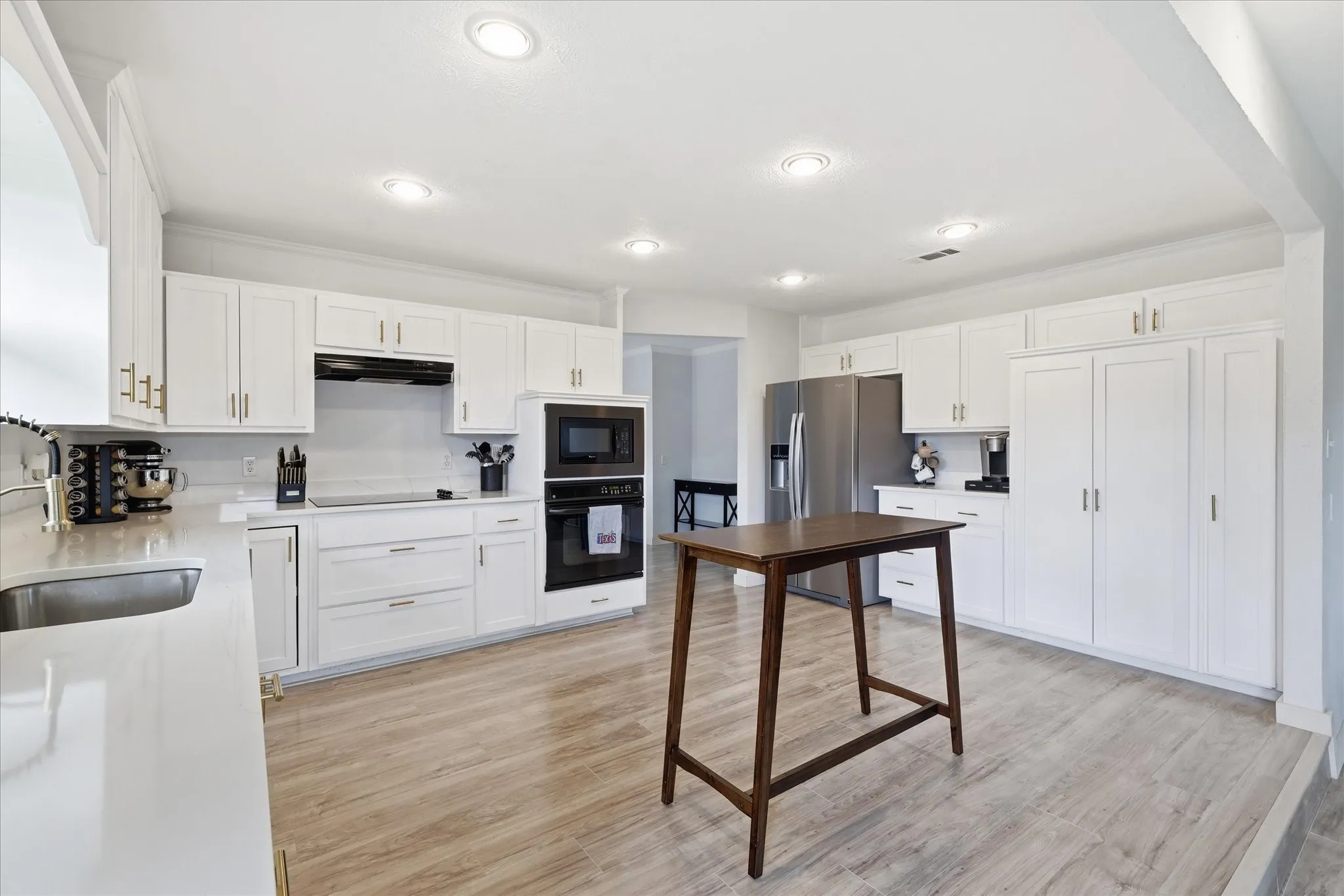 Bright kitchen featuring white cabinetry with gold-tone hardware, stainless steel appliances, a built-in oven and microwave, and wood-finish flooring