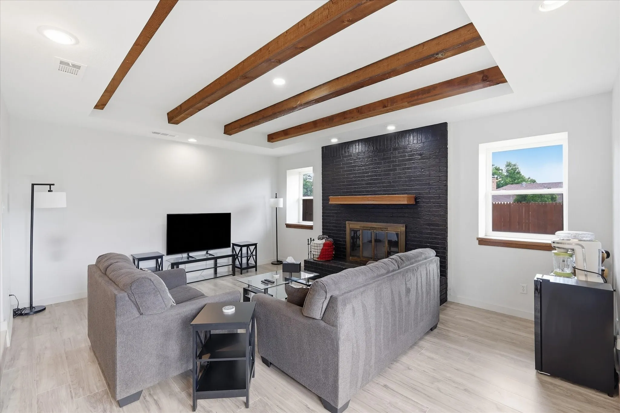 Spacious living area featuring a black brick fireplace with wood mantel, recessed lighting, wood-finish flooring, and exposed ceiling beams