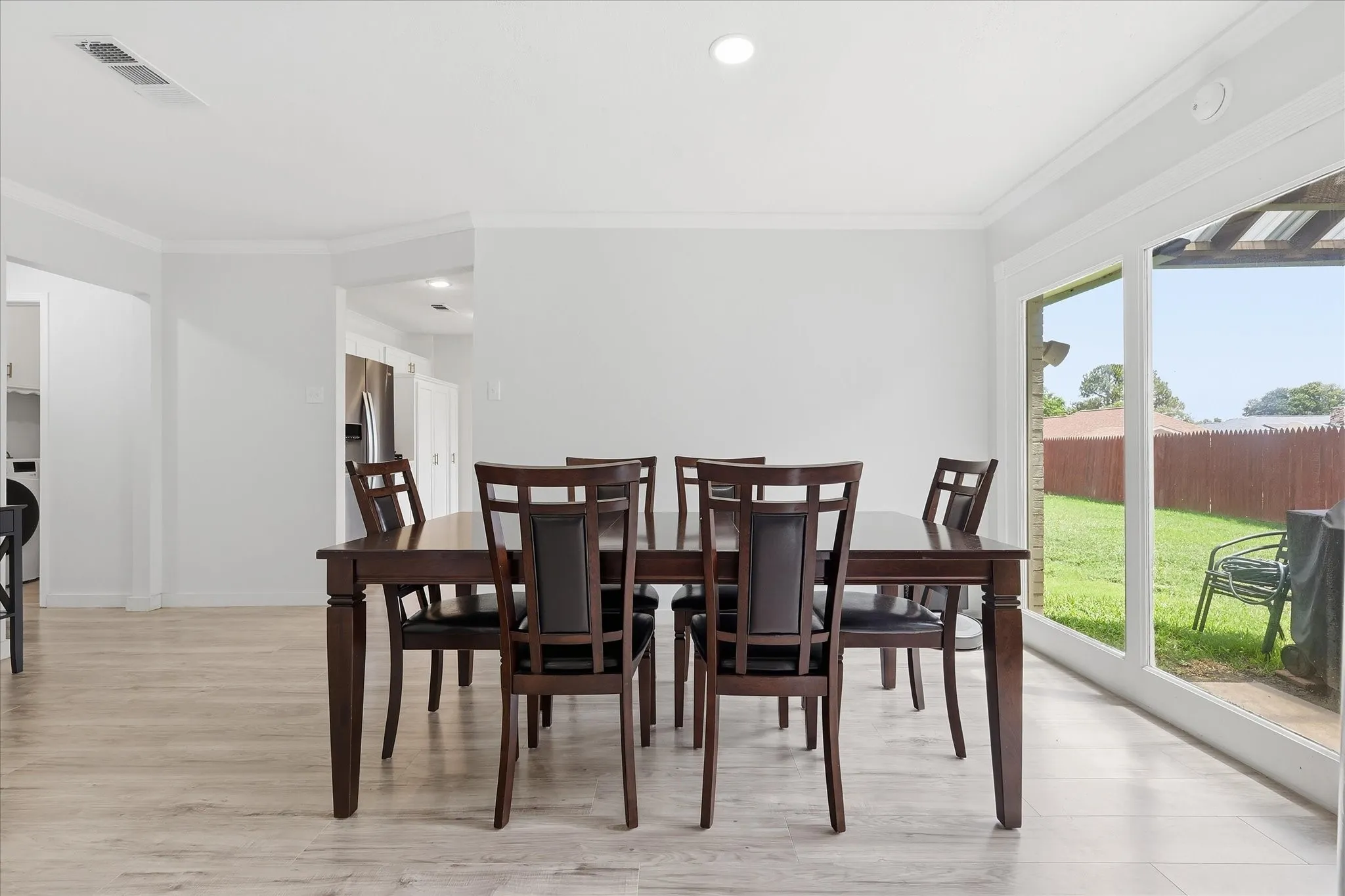 Dining area featuring light wood-finish flooring, white crown molding, recessed lighting, and a sliding glass door opening to an outdoor patio and yard