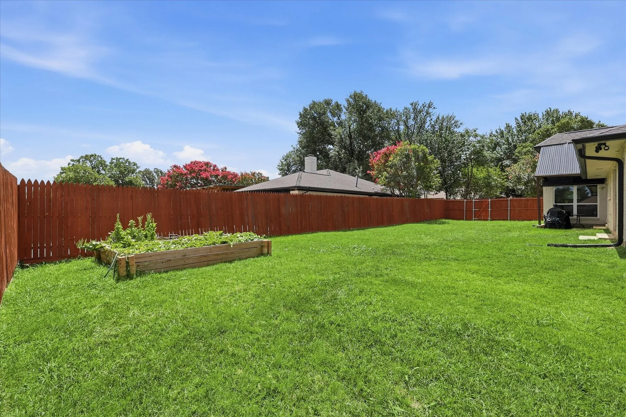 Expansive backyard featuring a manicured lawn, a full wooden privacy fence, and a raised garden bed