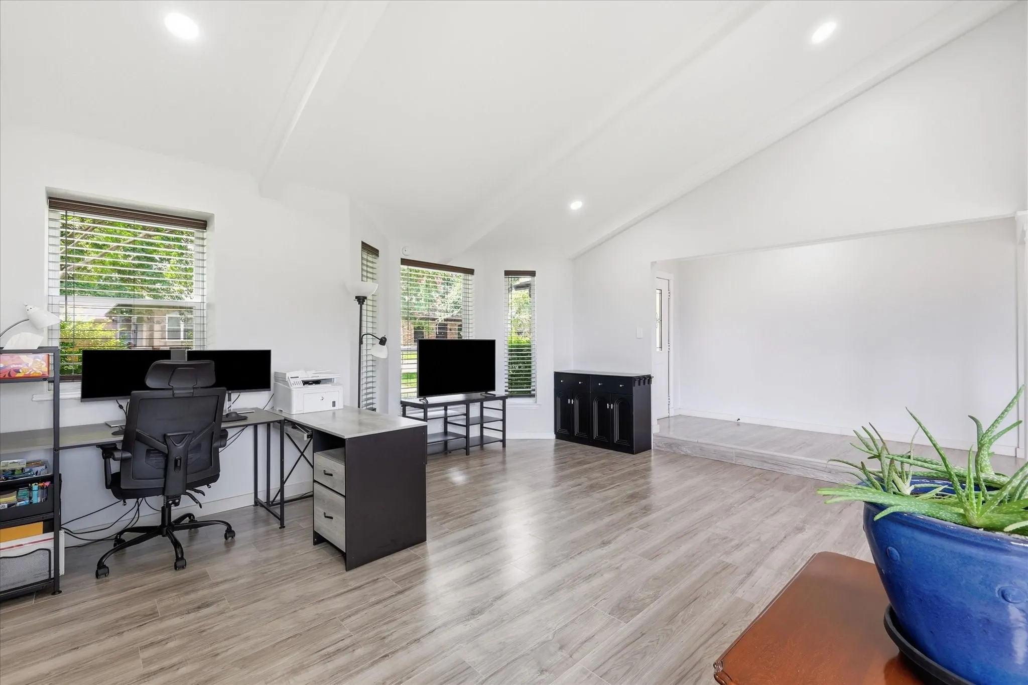Spacious living area featuring high vaulted ceilings, recessed lighting, wood-finish flooring, and multiple windows with blinds