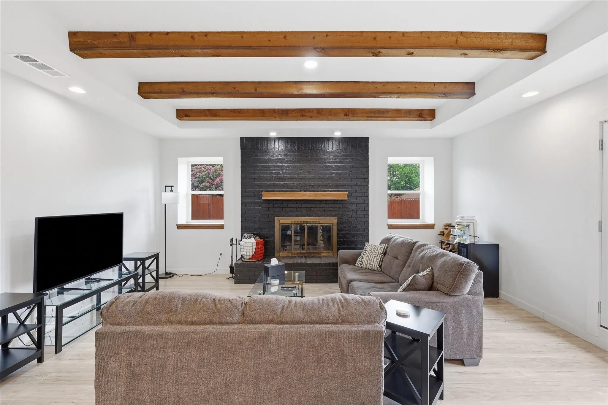 Spacious living area featuring a black brick fireplace, wood mantel, and light wood-finish flooring