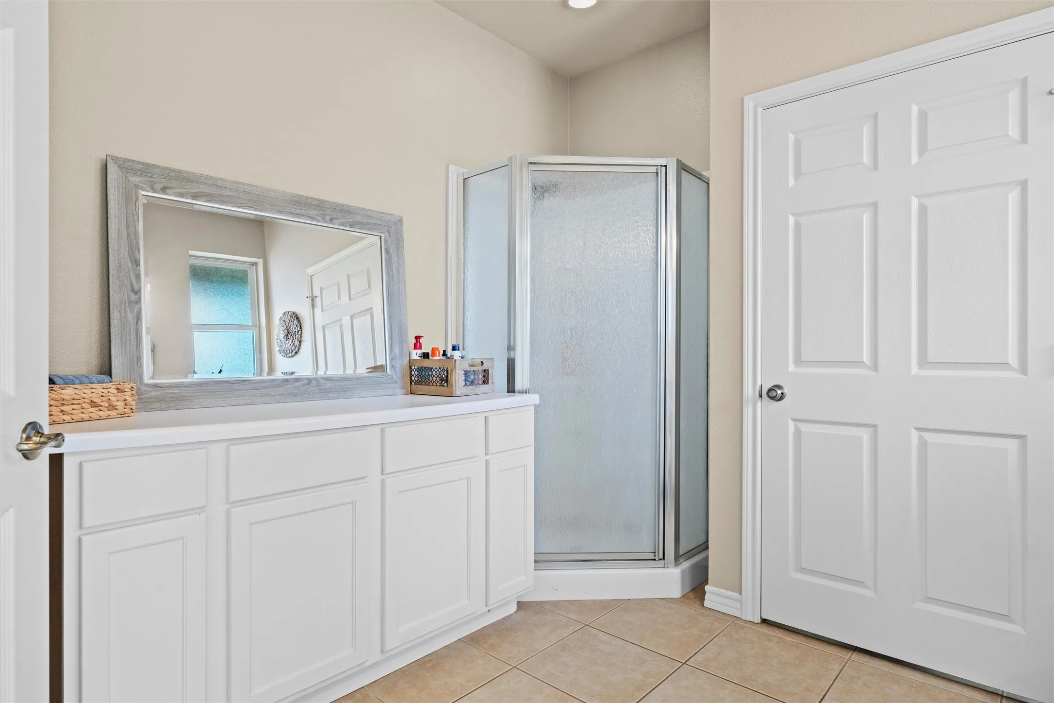 White cabinetry vanity with a light countertop, a framed mirror, and a corner shower with frosted glass