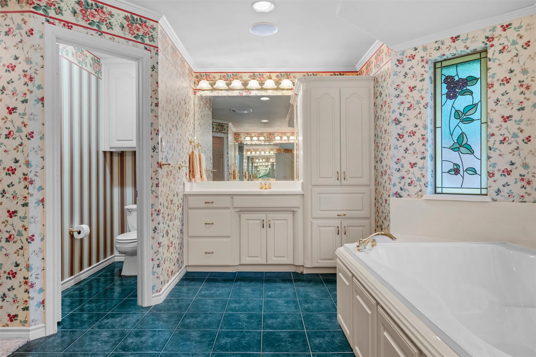 Bathroom featuring a white built-in soaking jetted tub, a stained-glass window, and a vanity with dual sinks. separate enclosed water closet.