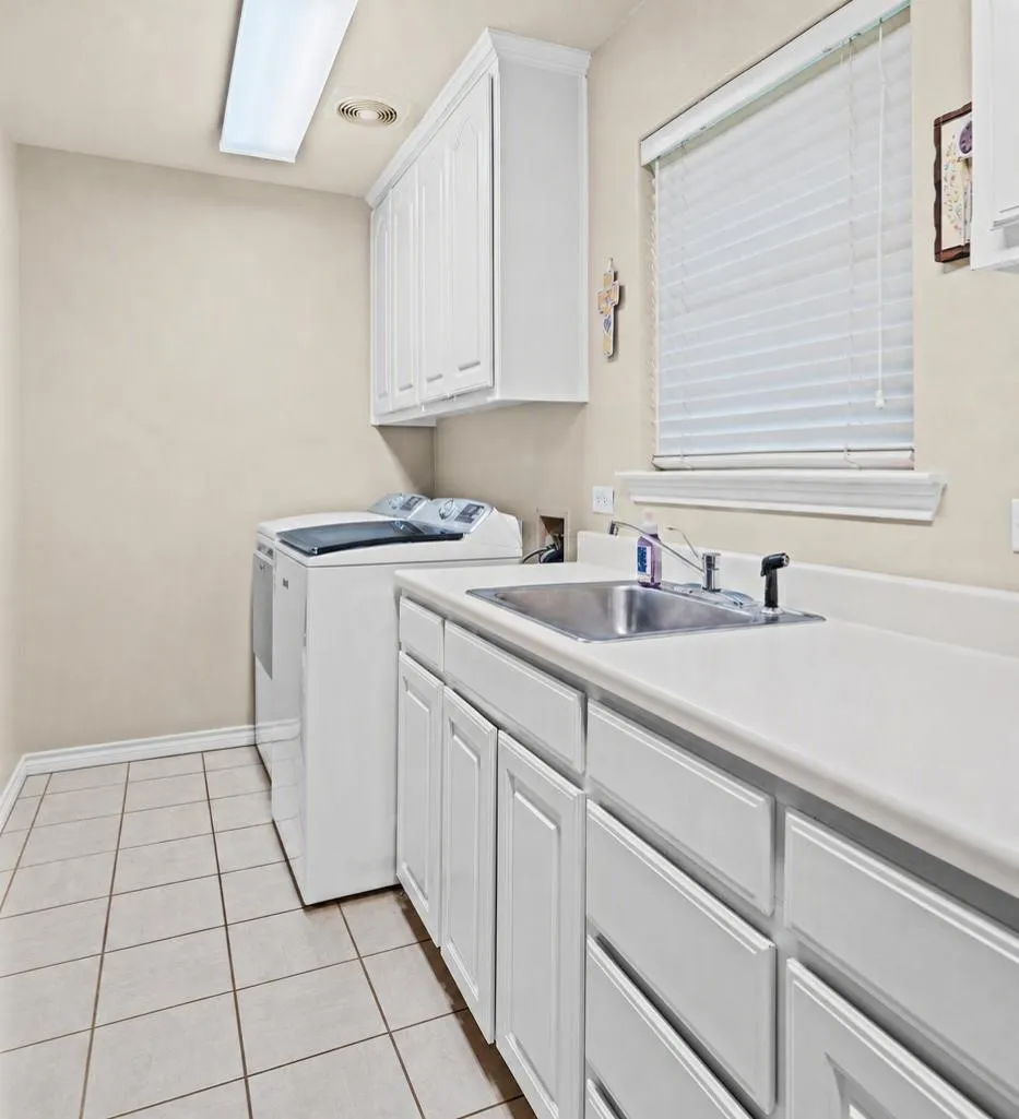 Laundry room featuring white shaker-style cabinetry, a stainless steel sink, light-toned countertop, and tile flooring
