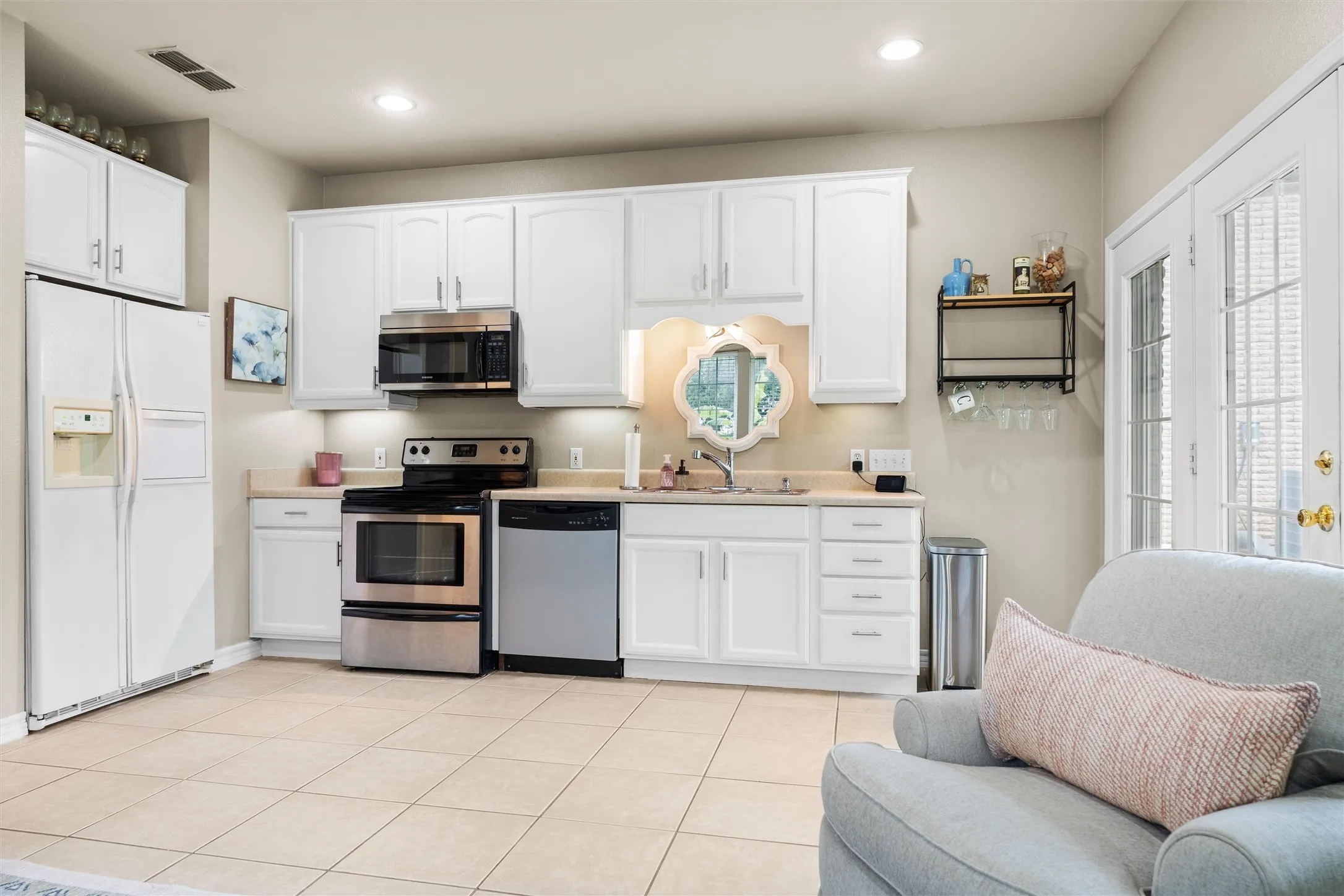 Bright kitchen featuring white cabinetry, light-toned countertops, stainless steel appliances and tile flooring.