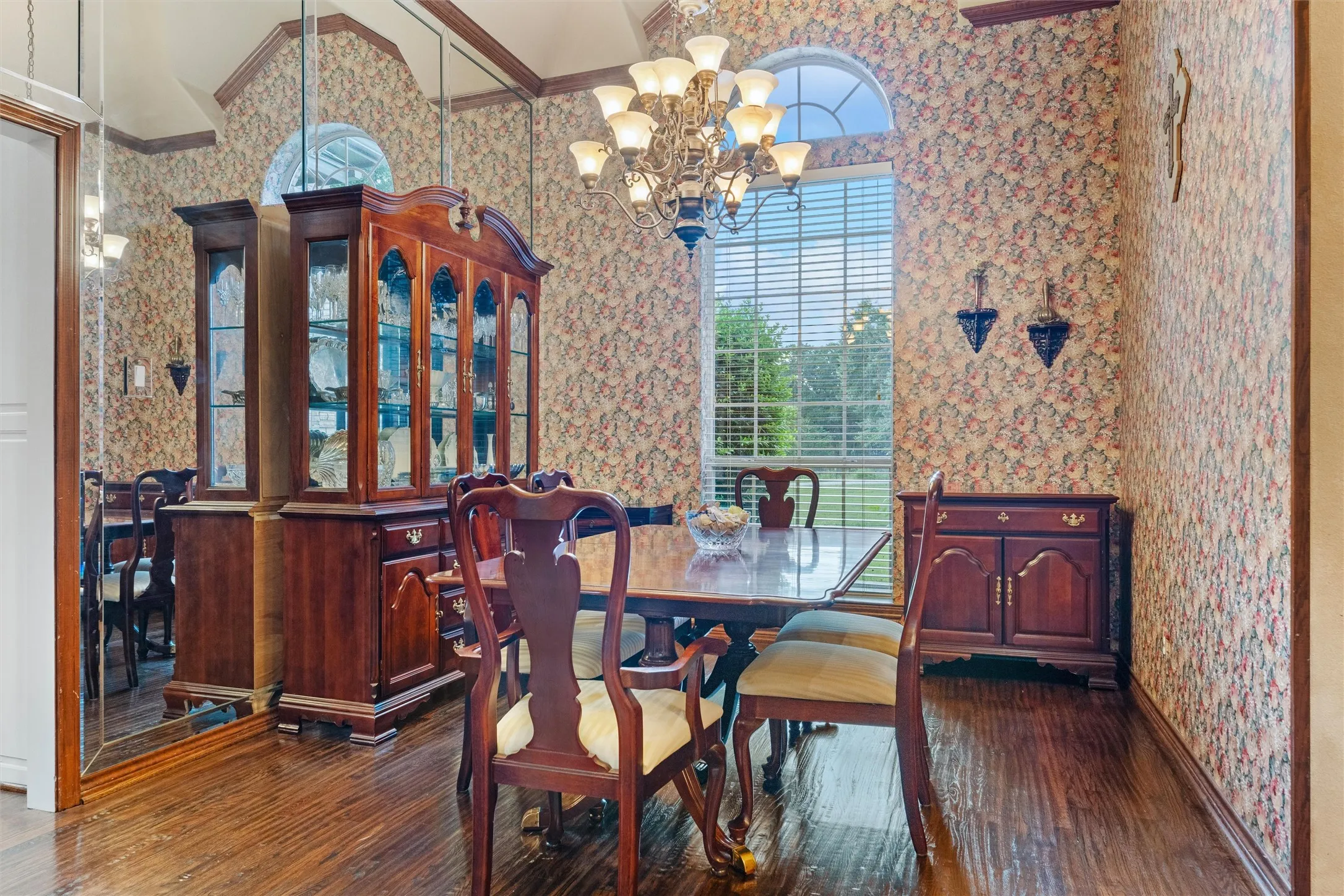 Formal dining area featuring rich wood-finish flooring, a large arched window with blinds, and a multi-tiered chandelier