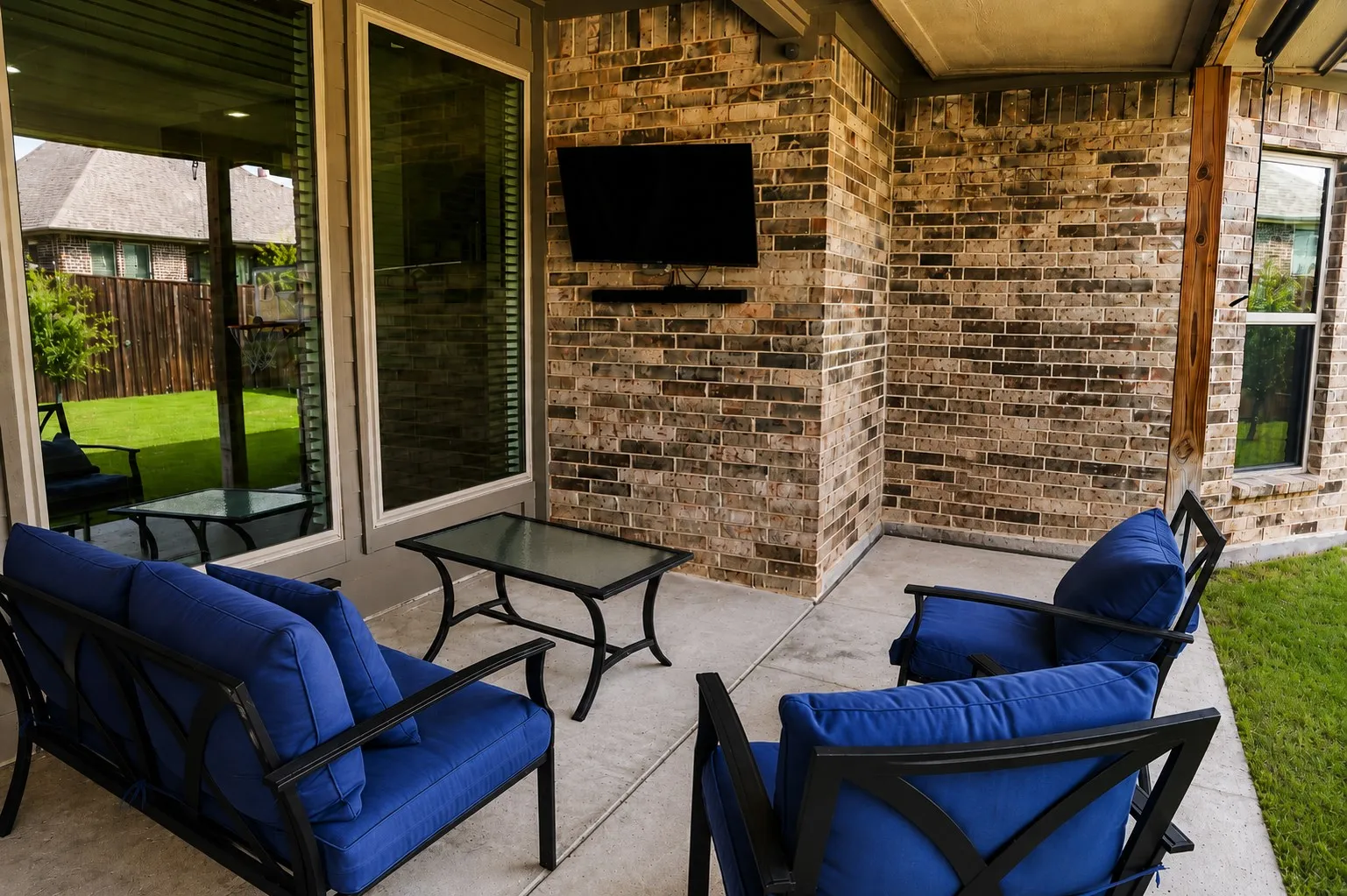 Covered patio featuring a brick accent wall, mounted television, and concrete flooring