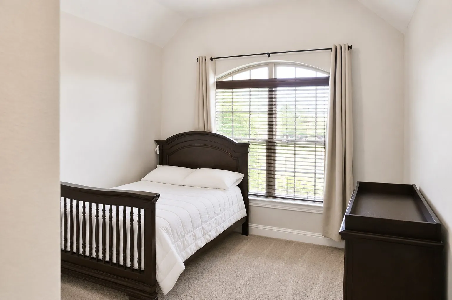 Vaulted ceiling bedroom featuring an arched window with blinds and drapes, and neutral carpet flooring